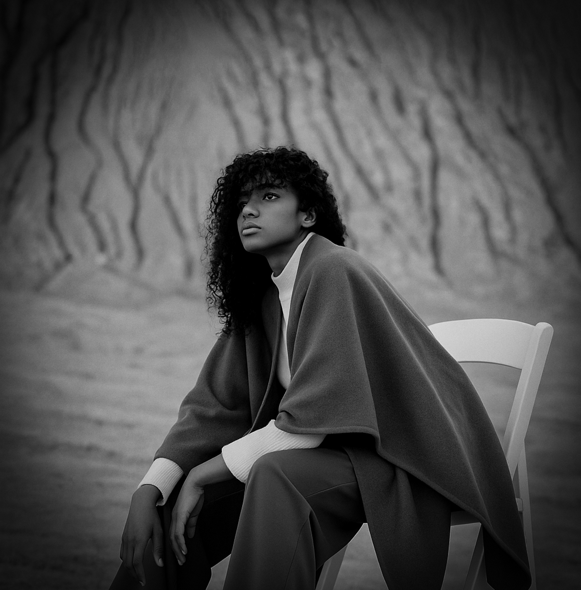 Elegant woman in a wide-brimmed hat, statement hoop earrings, and a flowing cape, captured in a black and white profile again