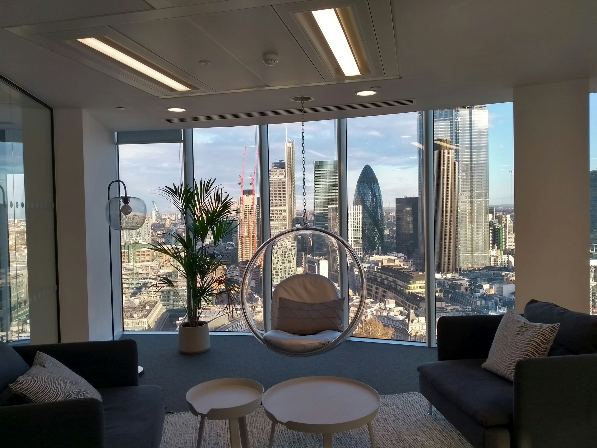Modern kontorslounge med bubbelfåtölj framför stort fönster med vy över Londons skyline och ikoniska Gherkin-byggnaden