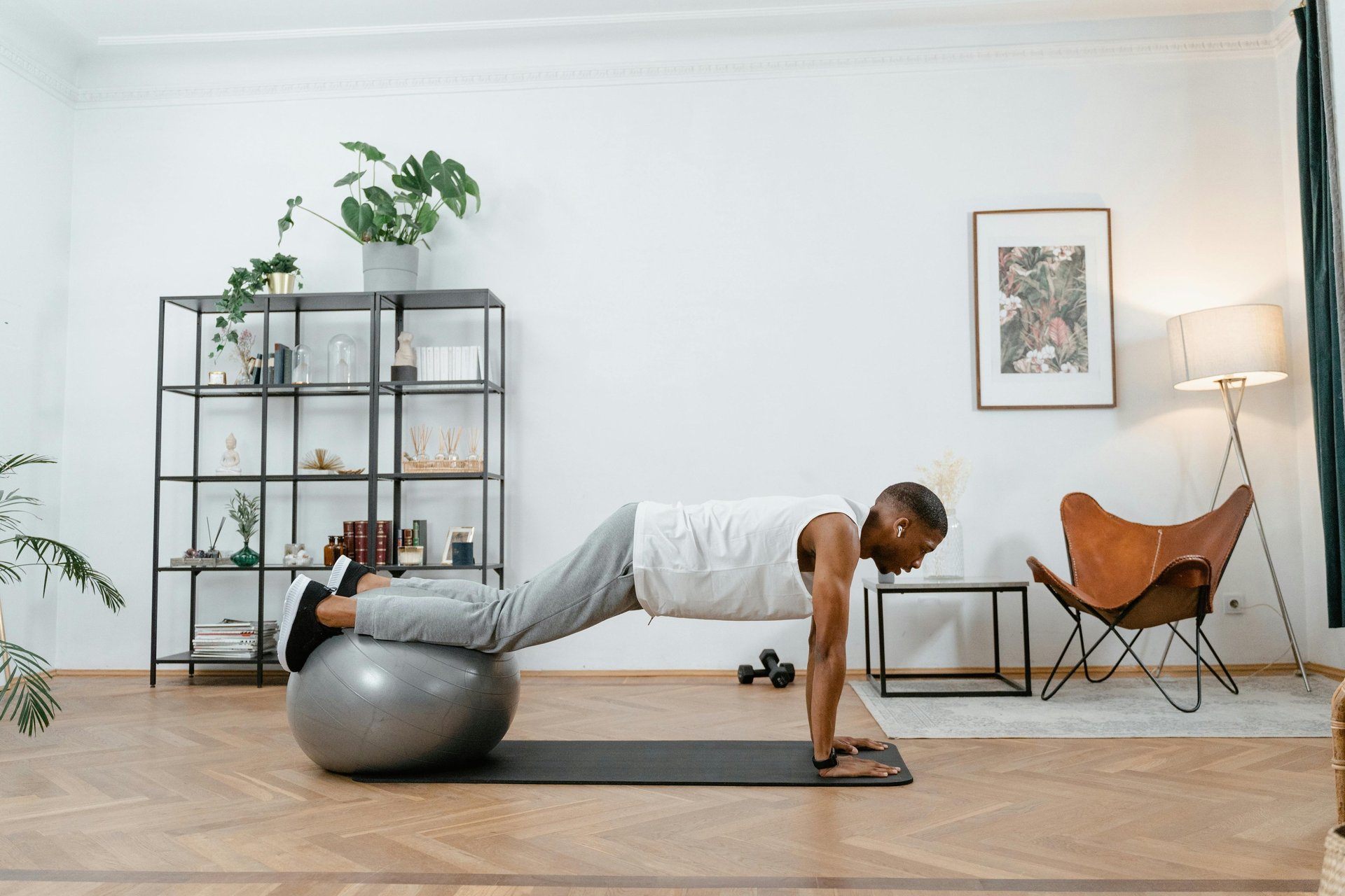 Hombre haciendo flexiones de pecho con los pies sobre un balón de estabilidad gris durante una clase de fuerza funcional de Y