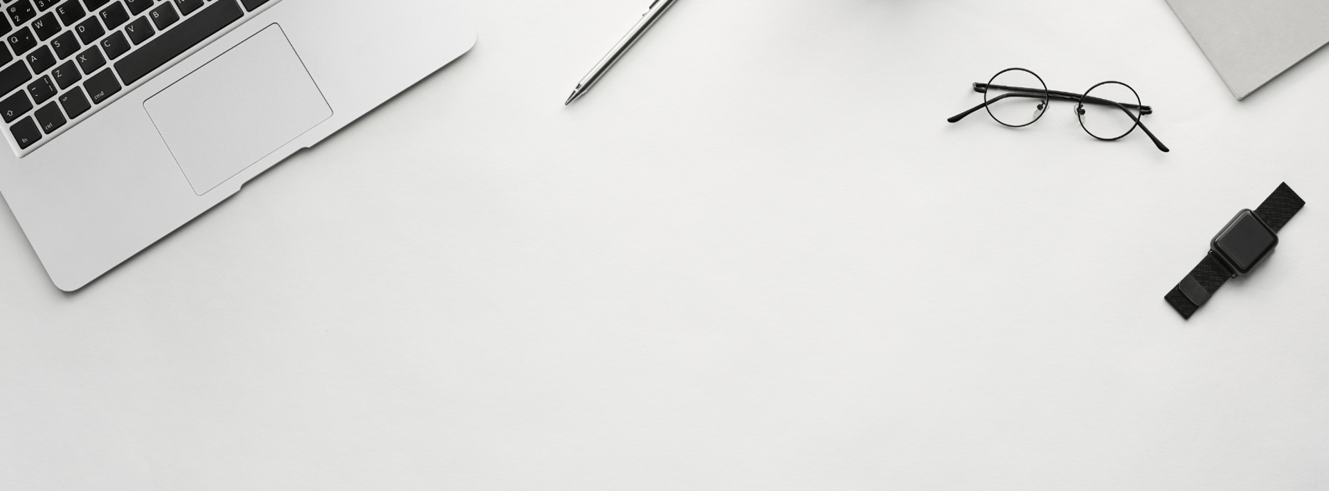 An open empty notebook on a white desk next to an iPhone and a MacBook