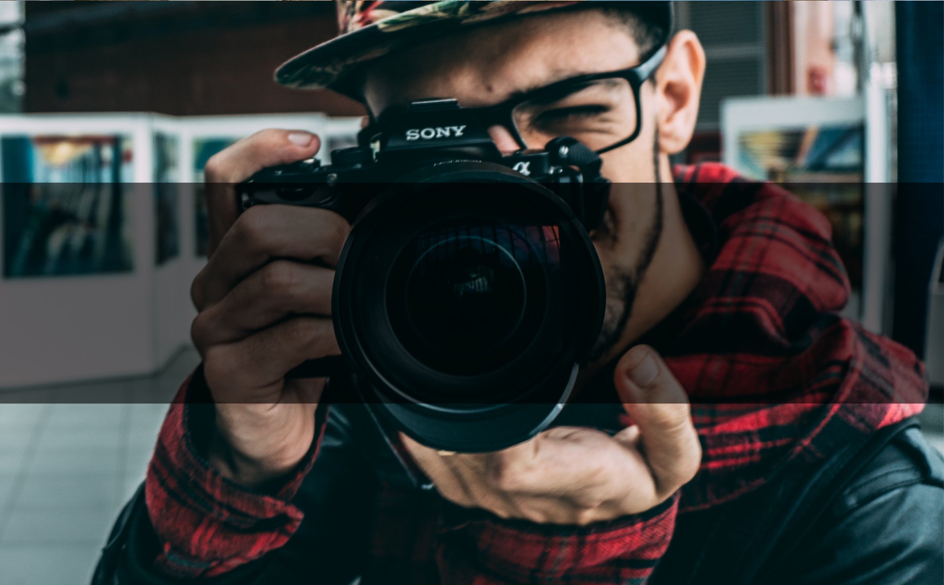 Un homme à lunette et casquette qui prend une photo avec bandeau noir 