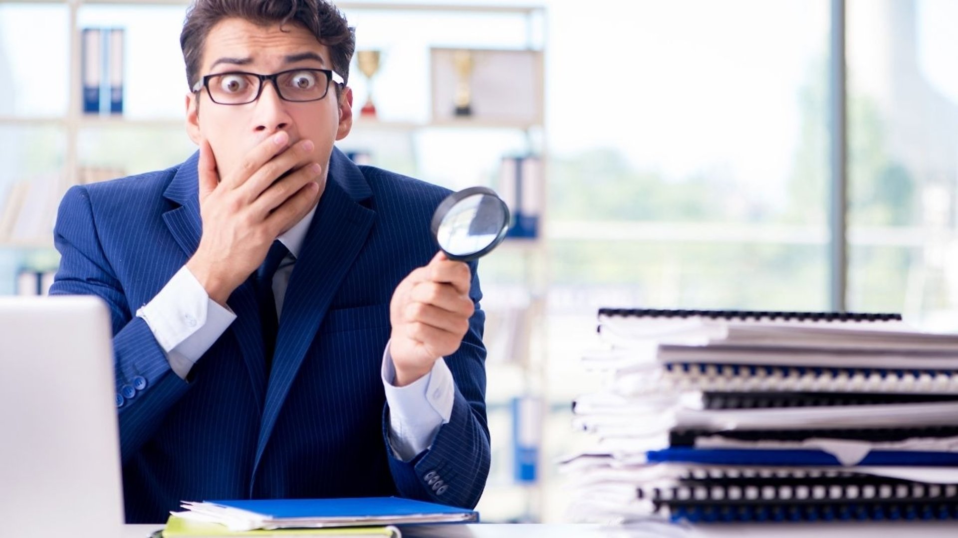 Un homme d'affaire choqué avec une loupe à la main sur son bureau 