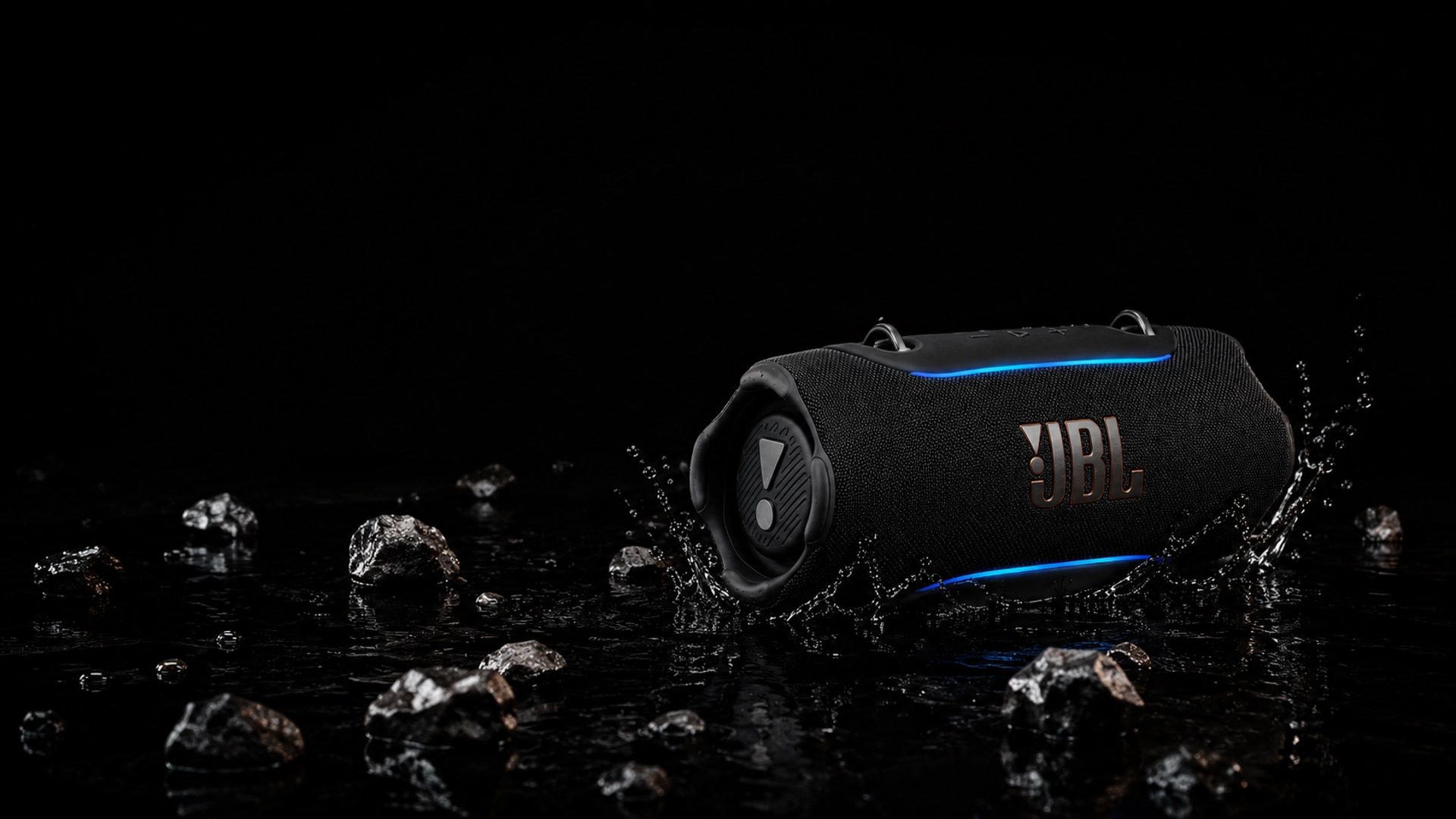 Enceinte Bluetooth JBL Xtreme 5 noire sur des rochers humides avec éclaboussures d'eau
