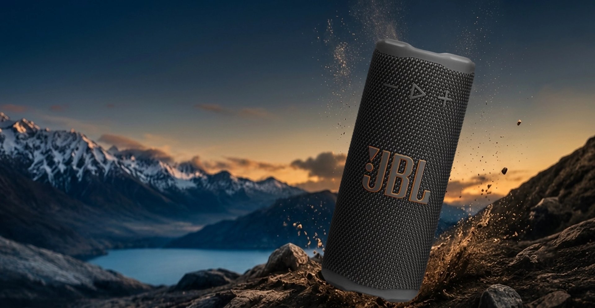 JBL GRIP sur paysage montagneux au coucher du soleil avec effet de projection de terre et pierres.