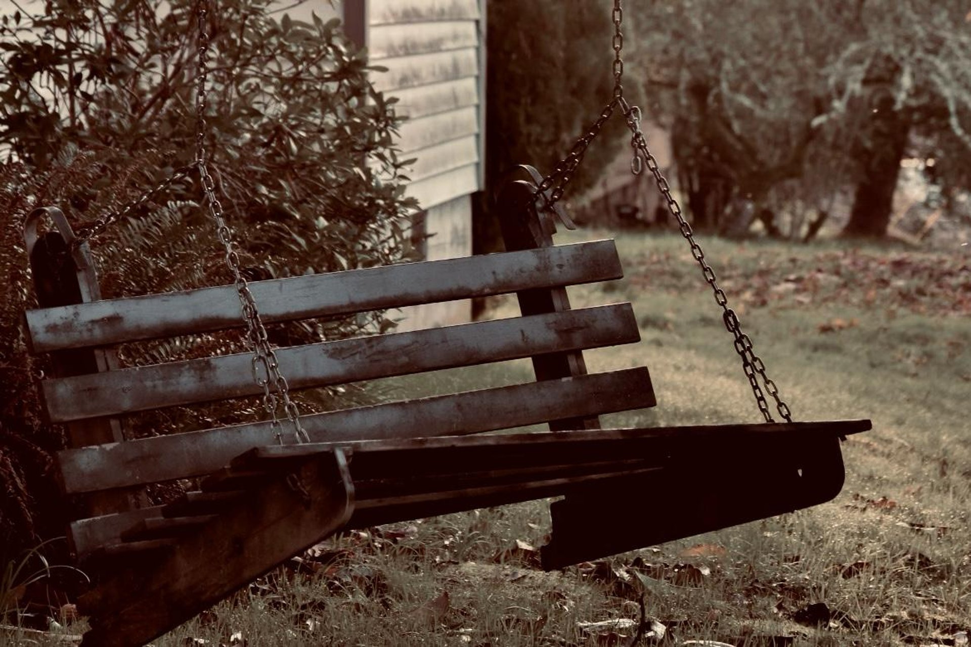 a wooden swing sitting in the grass next to a house
