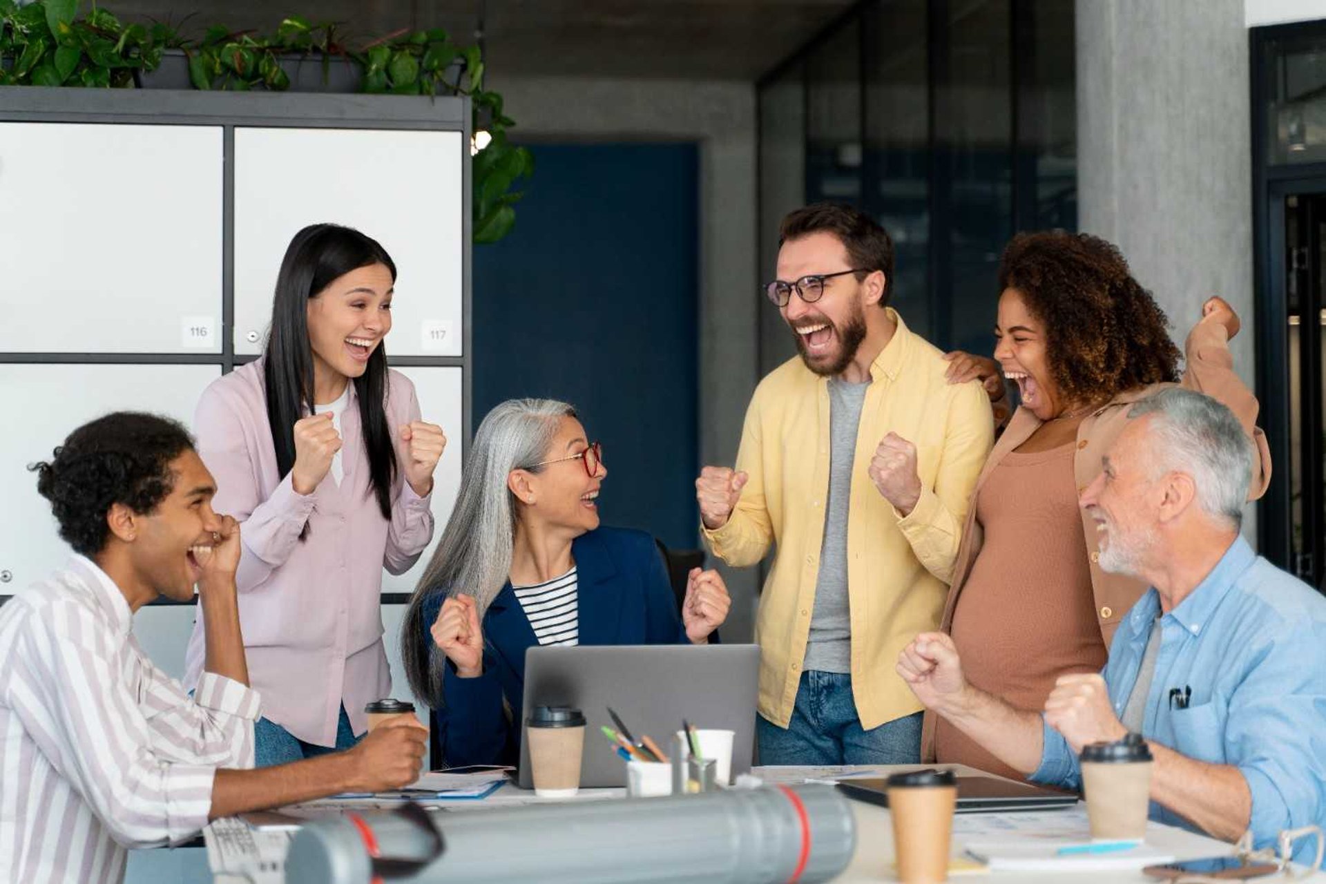 men and women sitting and standing while staring at laptop