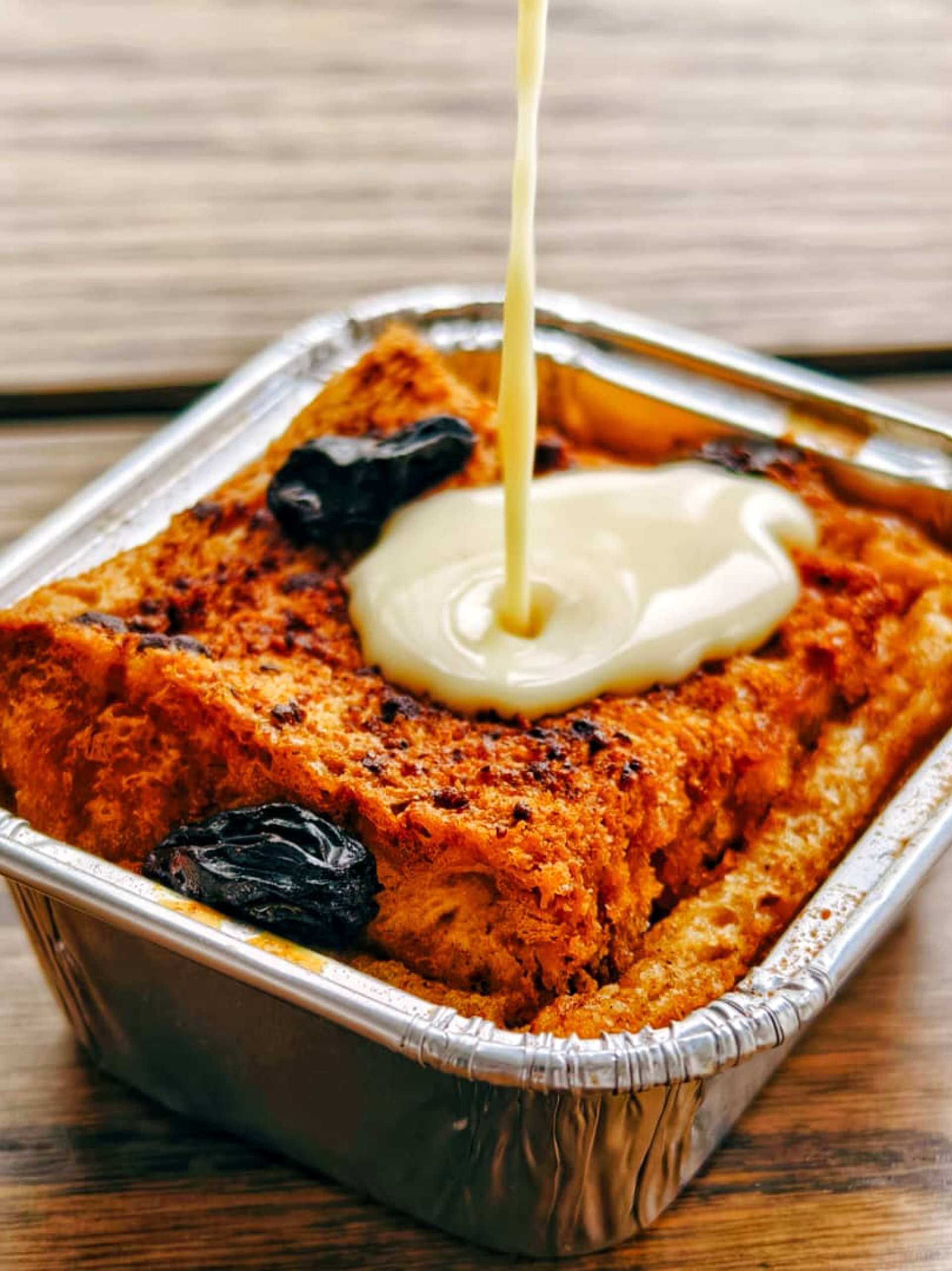 A crispy bread and butter pudding, with a steady stream of crème anglaise being poured over it.