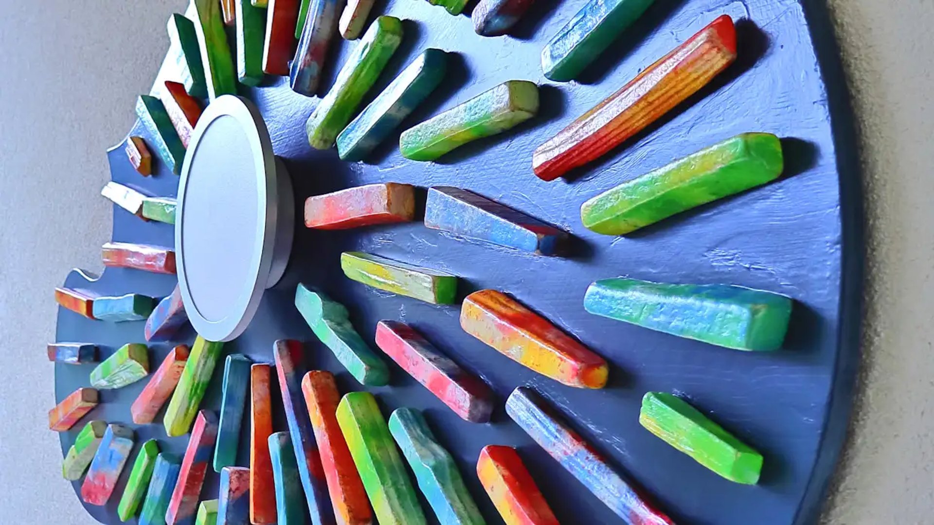 Nahaufnahme des real gewordenen Wandbildes aus sternförmig verklebten, bunten Holzscheiten mit integrierter Wandleuchte