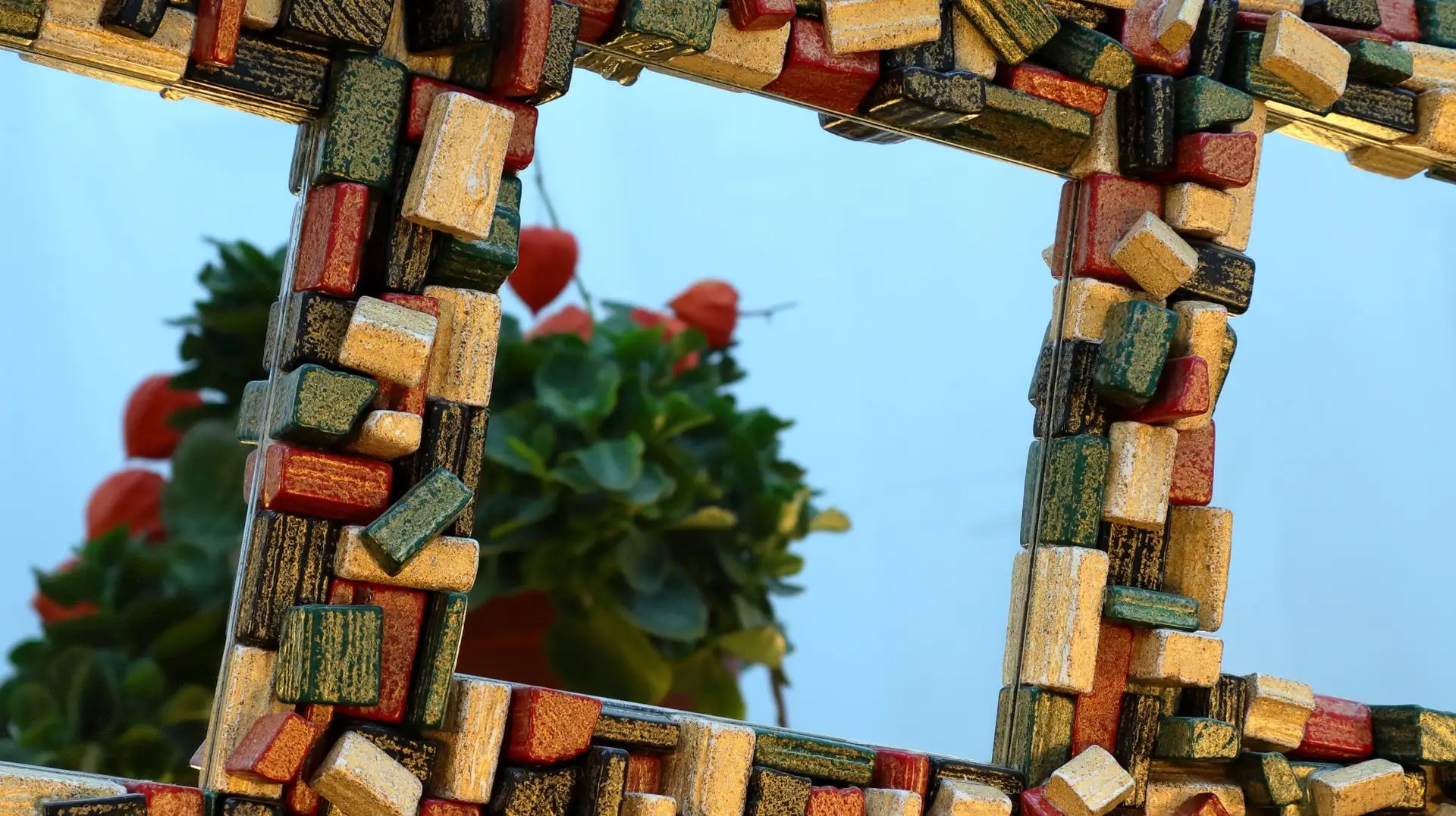 Nahaufnahme eines eleganten Spiegel-Unikats mit einem Rahmen aus schwarzen, grünen, goldenen und roten Holzscheiten