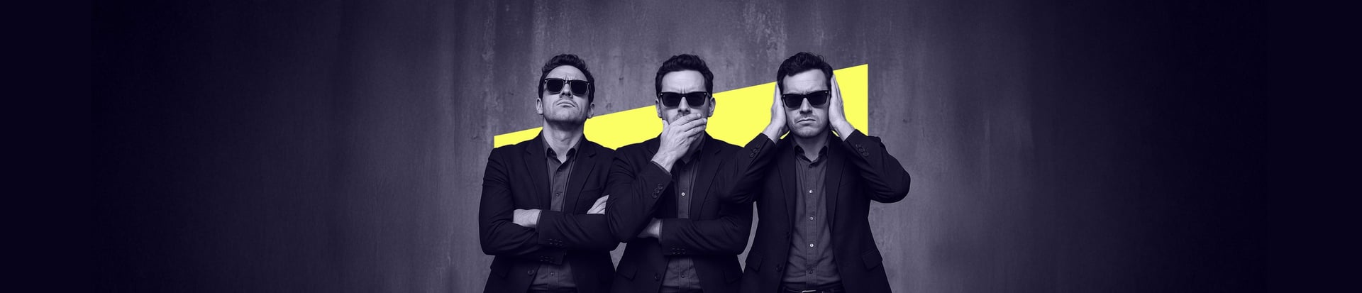 Three men in dark suits and sunglasses stand side by side against a grey wall with a yellow stripe, each striking a different