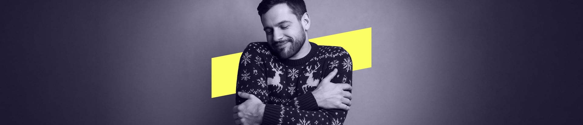 A man wearing a festive jumper hugs himself with a calm, contented smile. A yellow background shape.