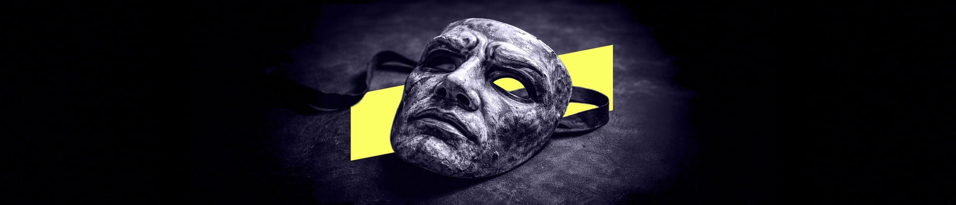 A worn theatrical mask lying on a dark surface with its ribbon undone.