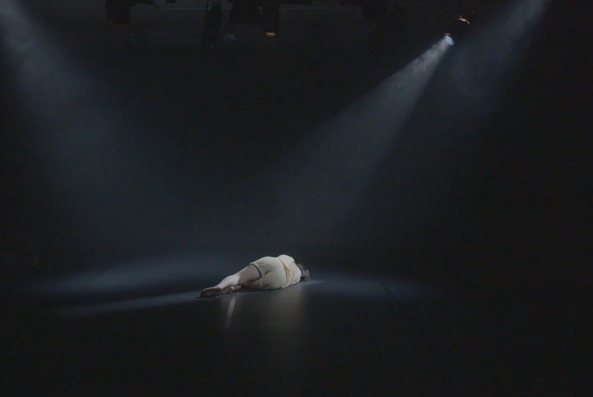 Dark stage with single spotlight illuminating performer – film still from Lingua Materna by Tina Bikic