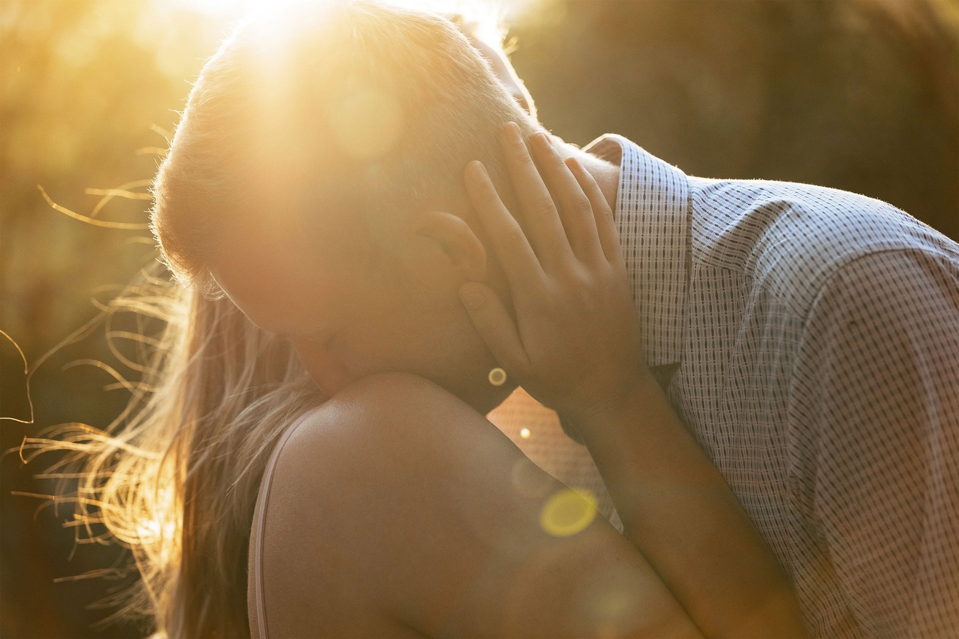 Una coppia durante una sessione fotografica di coppia al tramonto. lei lo abbraccia e lui le bacia una spalla