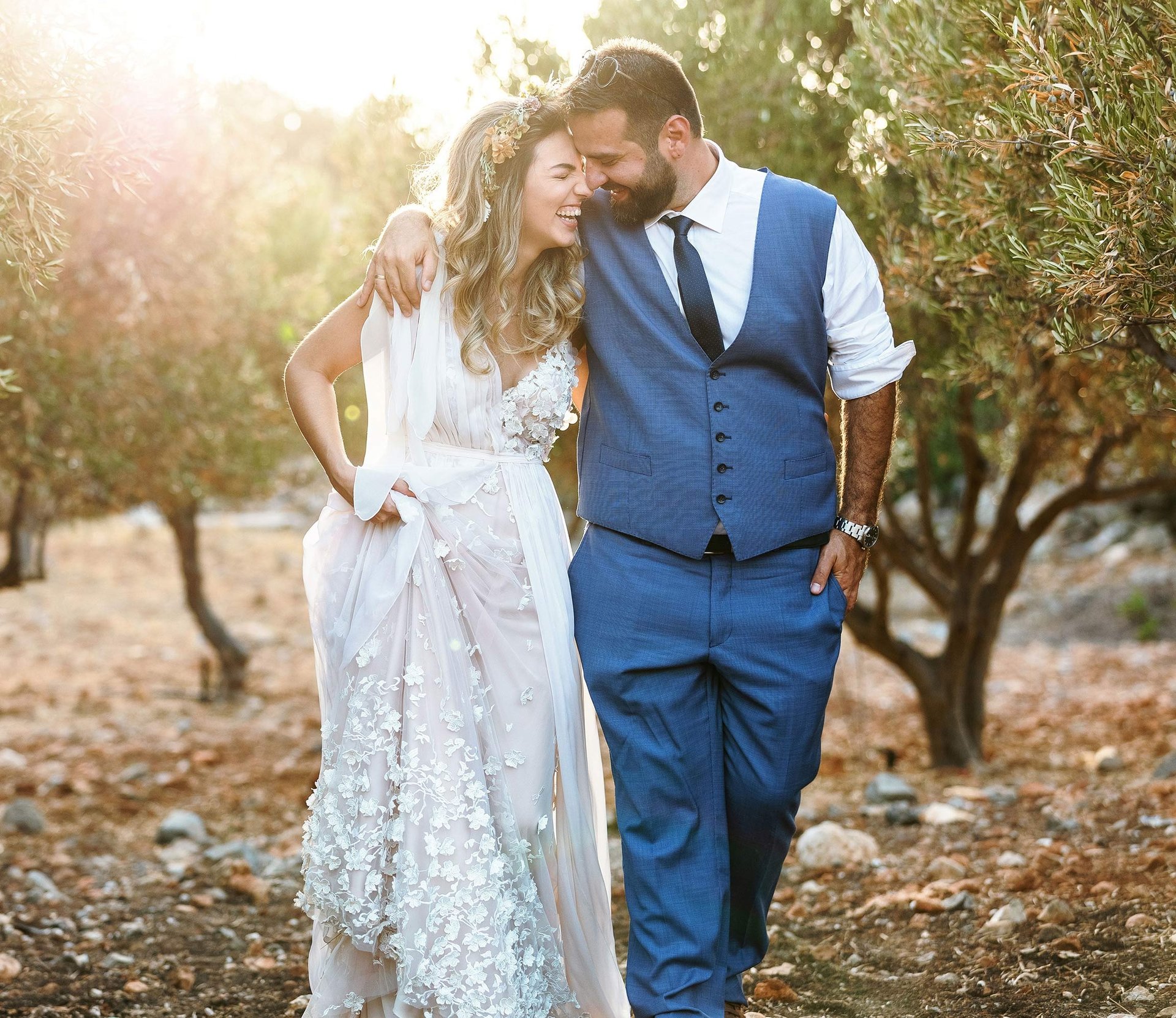 Una coppia di sposi cammina tra gli ulivi abbracciandosi e ridendo allegramente