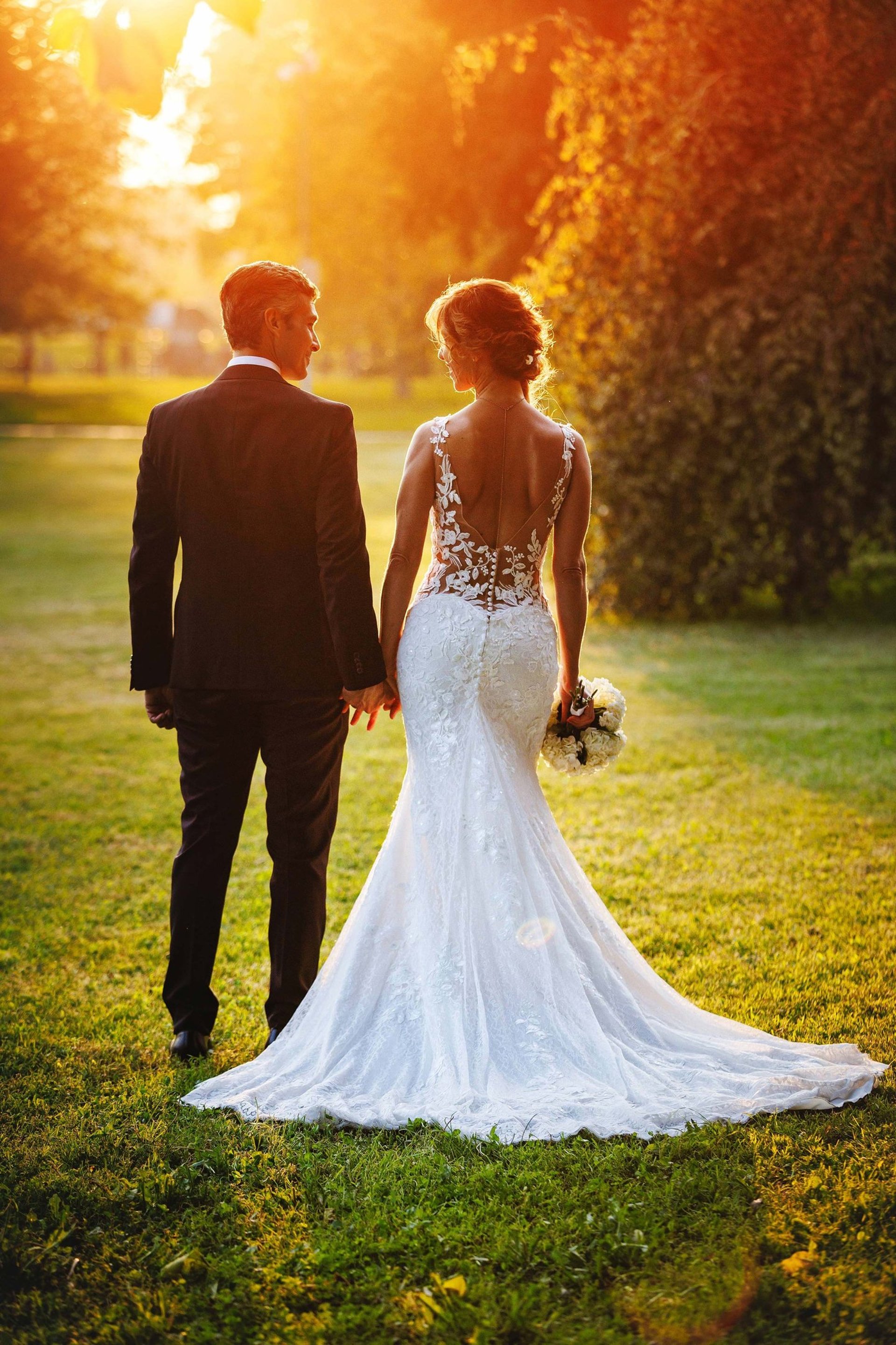 Una coppia di sposi inquadrati di spalle, si tengono per mano in un parco al tramonto