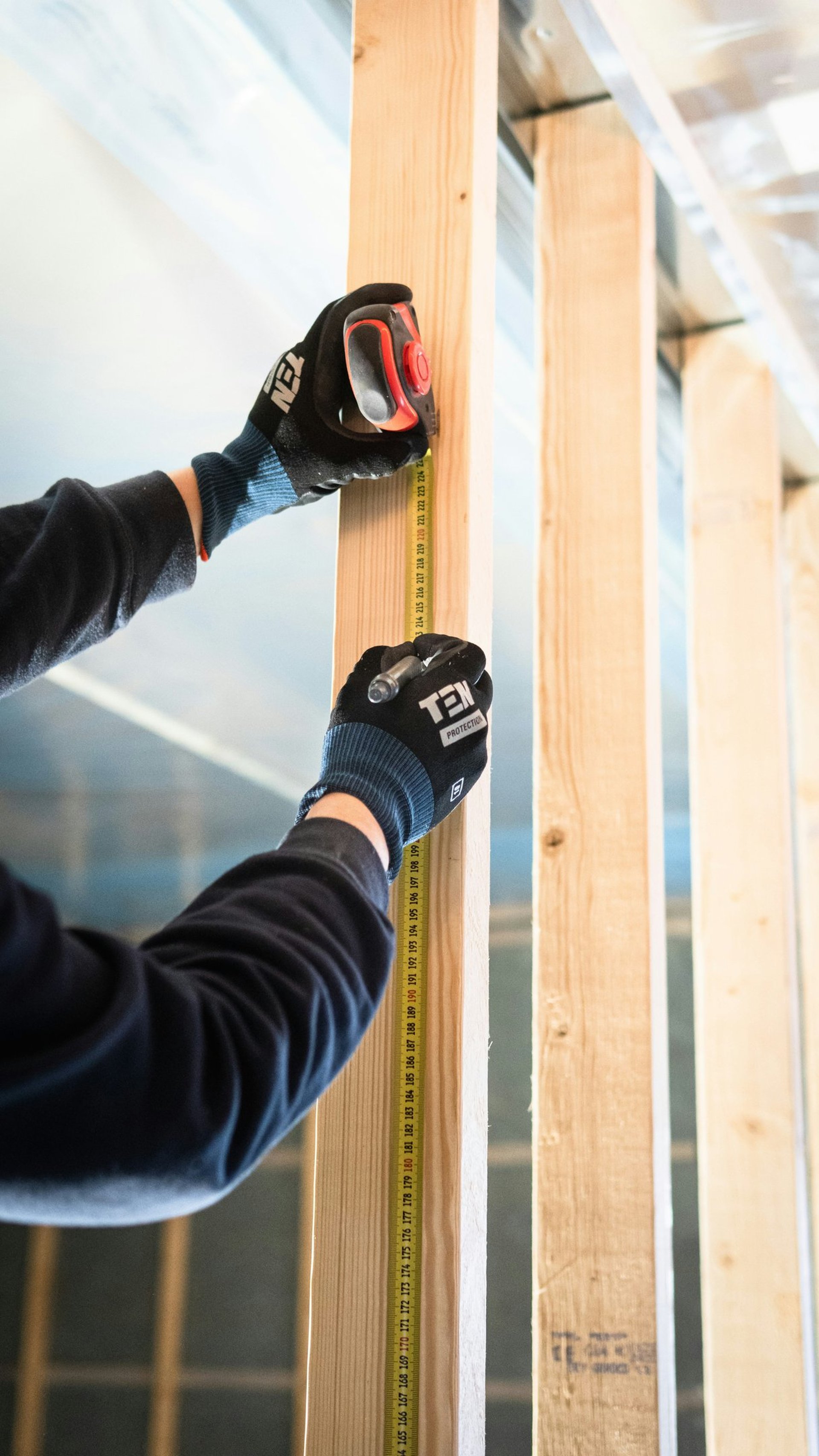 Professional builder wearing gloves, using a measuring tape to accurately measure a beam, on a construction site.