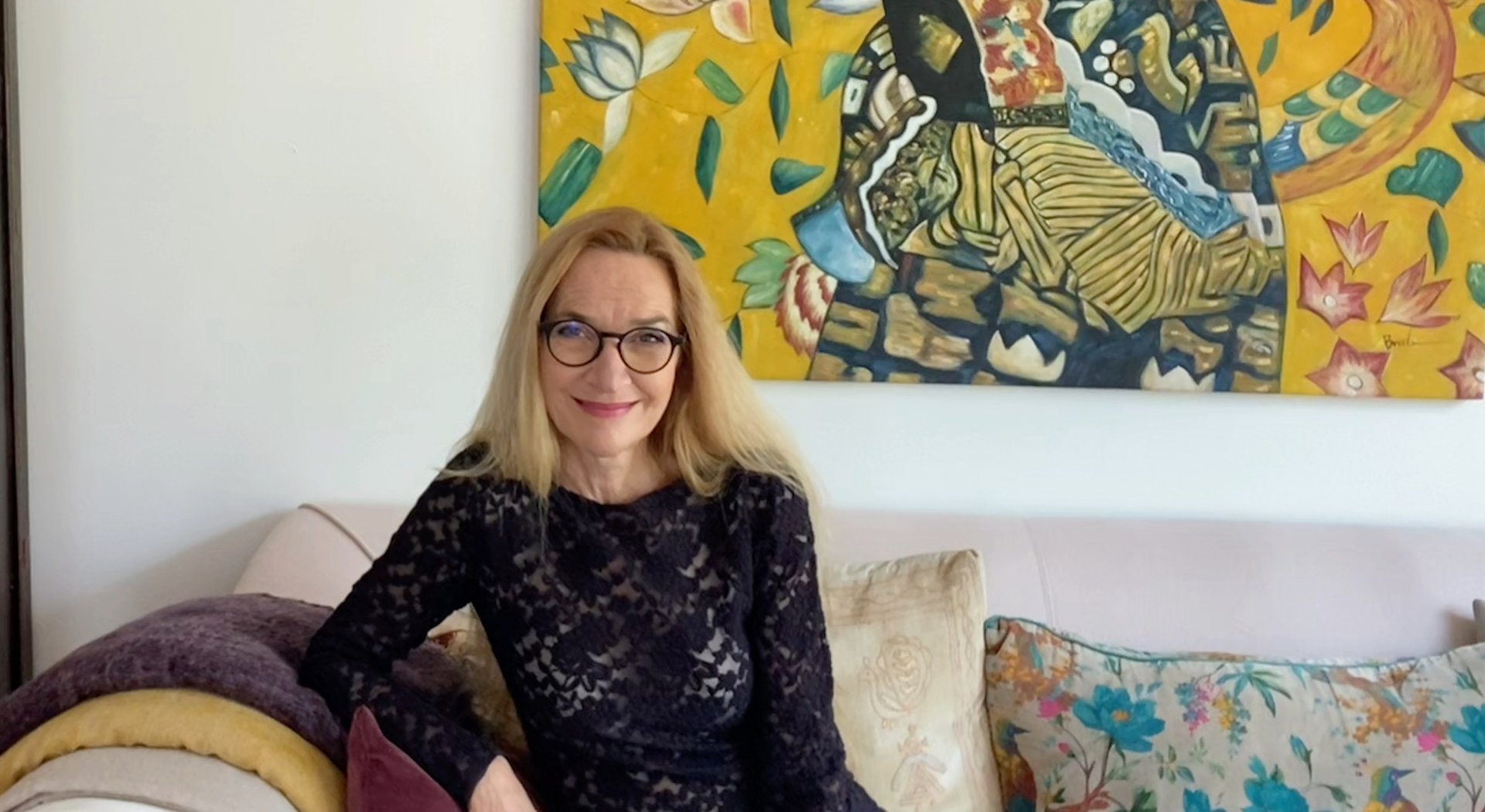 Porträt von der Affirmations-Expertin Die Wunderin, sitzend vor einem farbenfrohen Kunstwerk