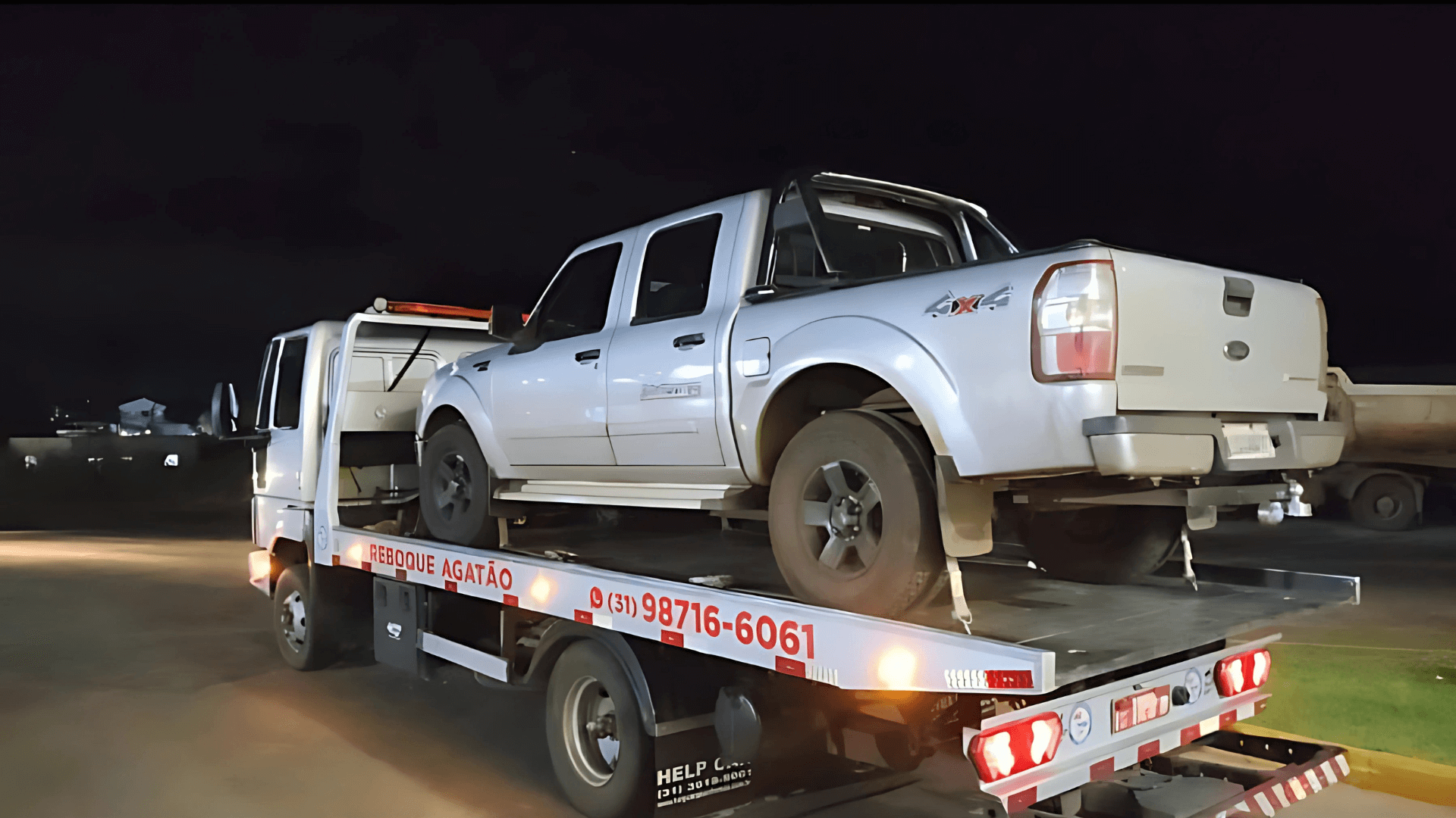 Guincho Agatão realizando transporte de caminhonete Ford prata à noite, com número de WhatsApp visível na lateral do caminhão