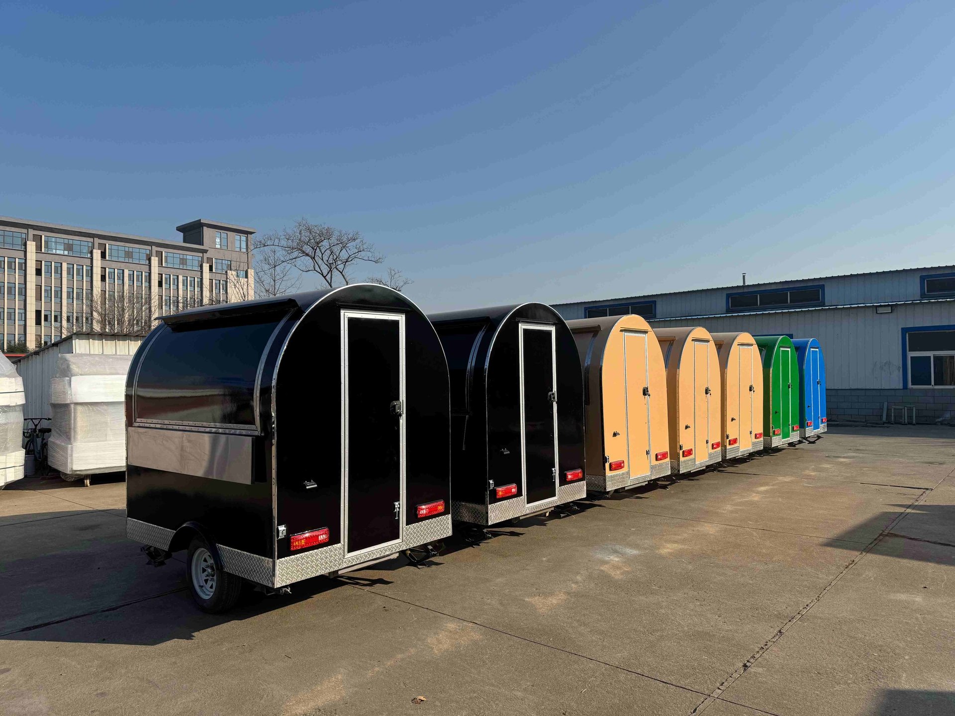 Foodtrucks demi-ronds TF-DM Classic alignés, disponibles dans plusieurs couleurs RAL : noir, bleu, beige, vert et rouge, pers