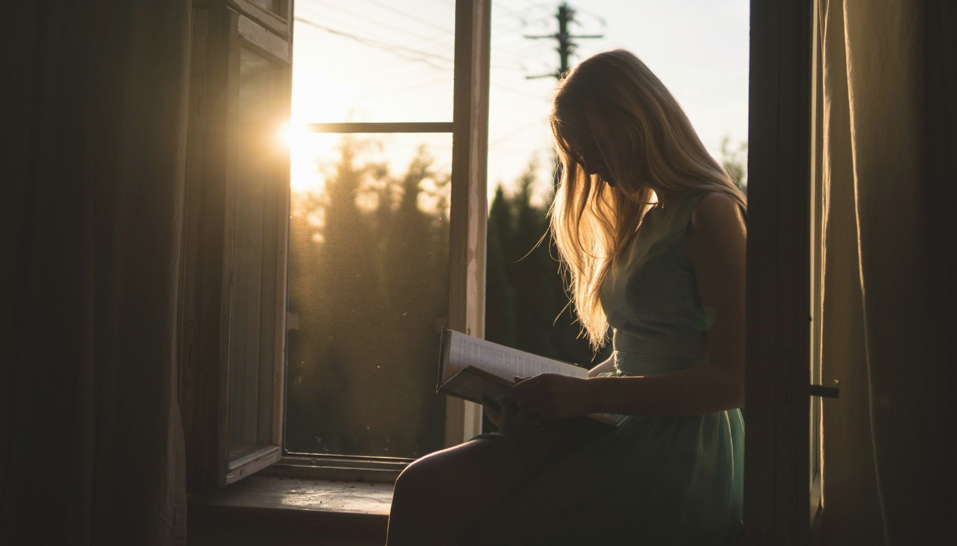 young blonde woman reads while sitting next to window