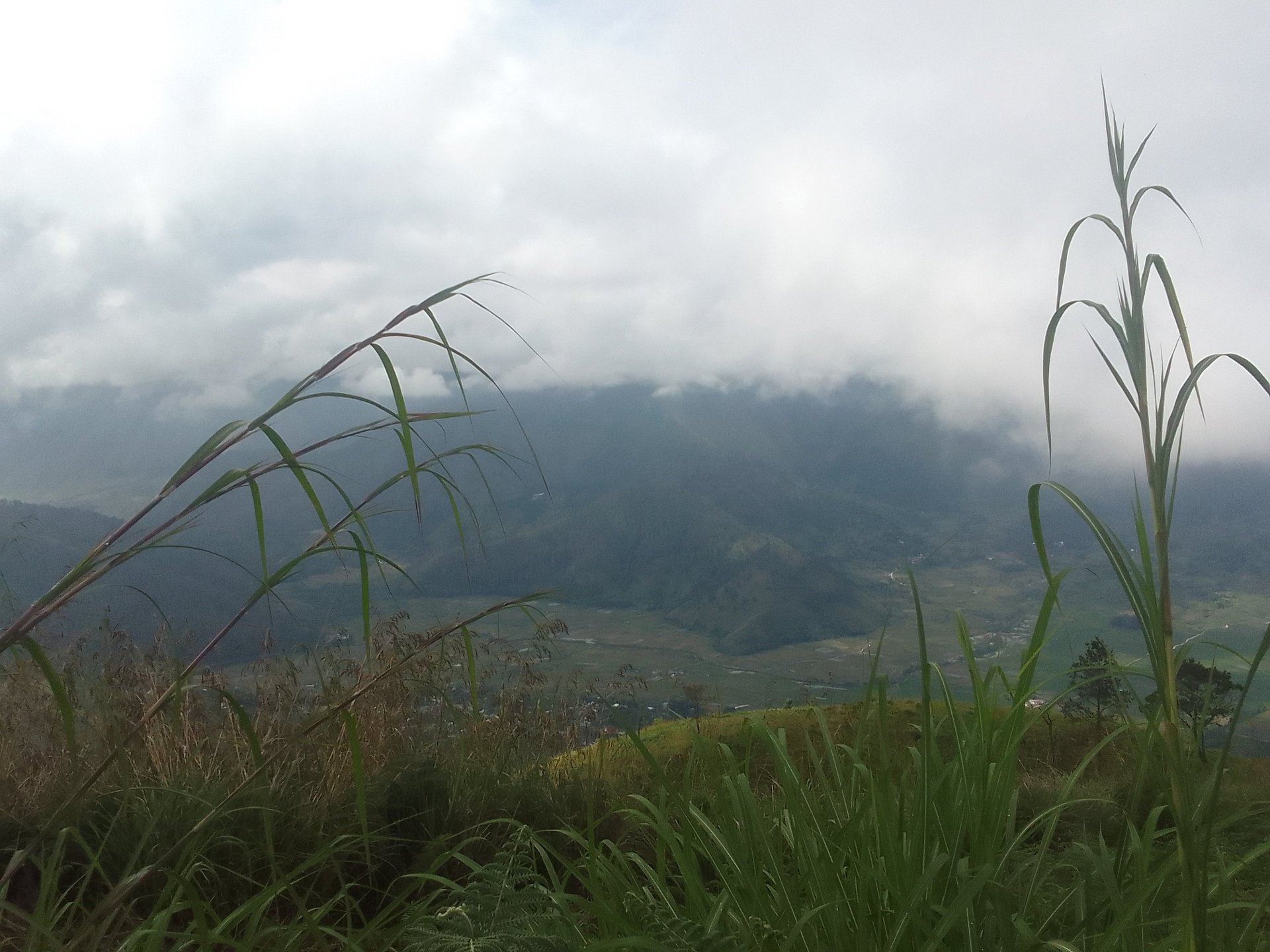 A photo looking down from a mountain into a valley with heavy cloud cover overhead