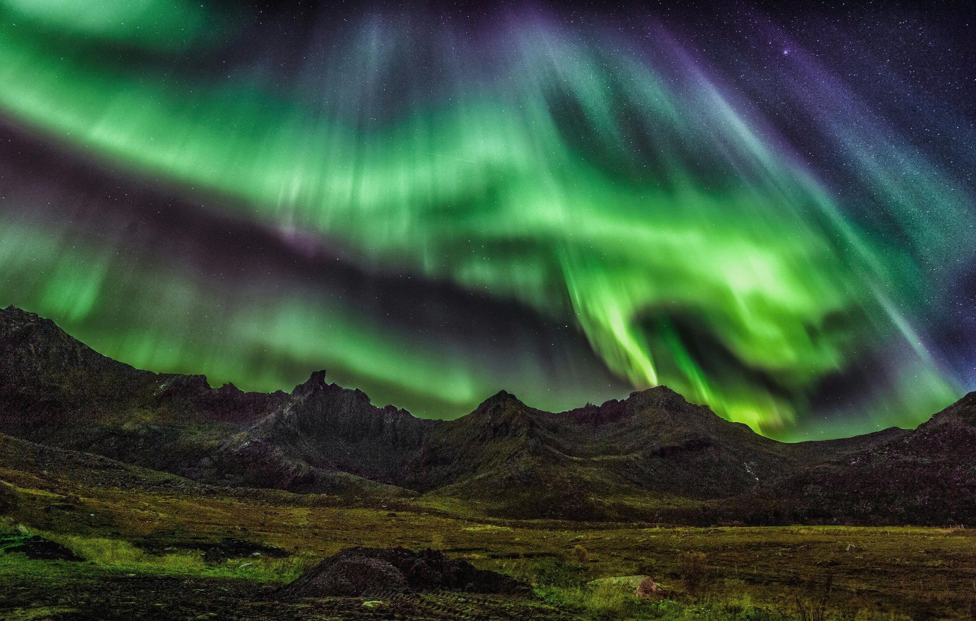 the northern lights appearing in green over a rugged mountainous landscape
