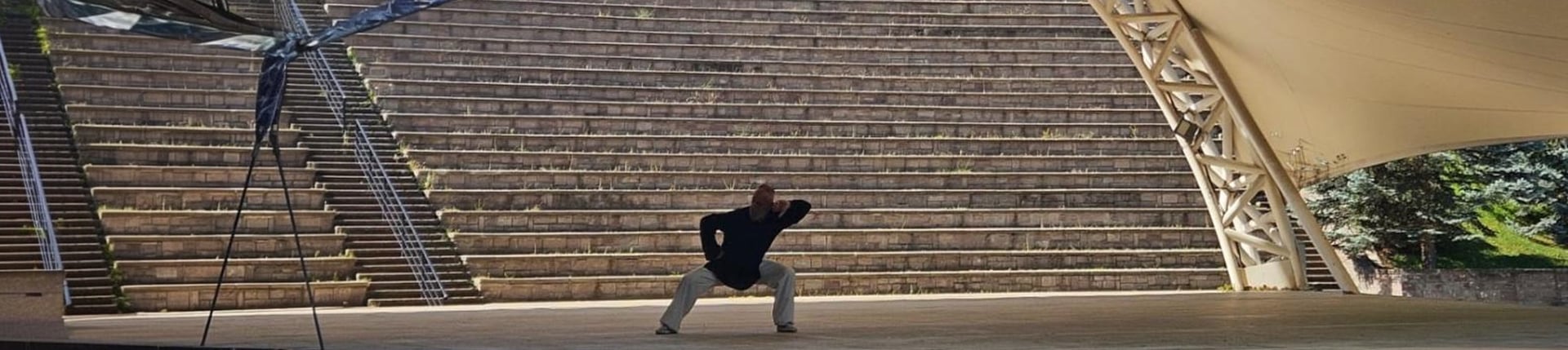 Harun Mehmet Soydan practicing Tai Ji solo on an open-air amphitheater stage under tensile roof.