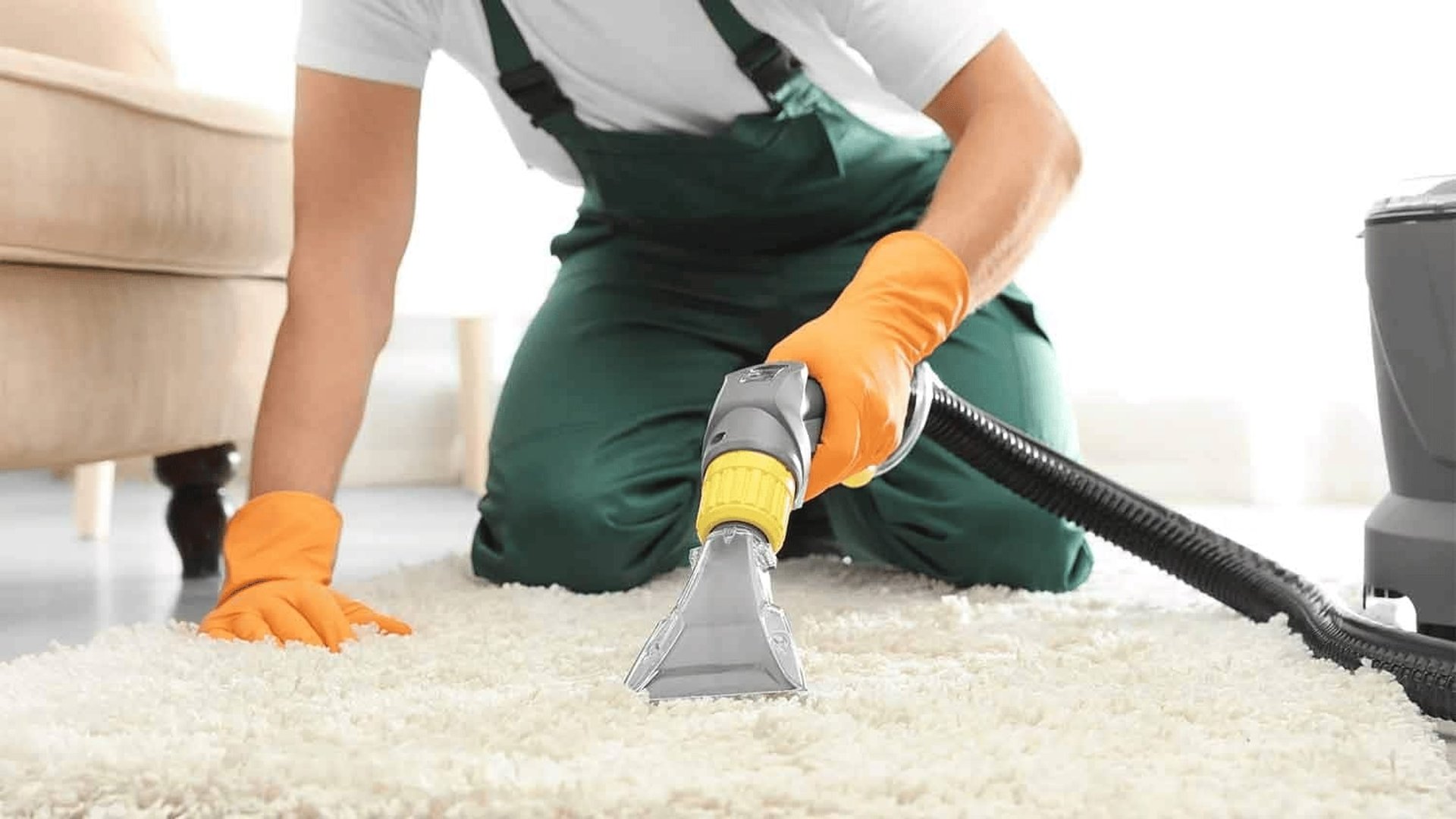 a woman in a green shirt and black gloves vacuuming a gray ottoman
