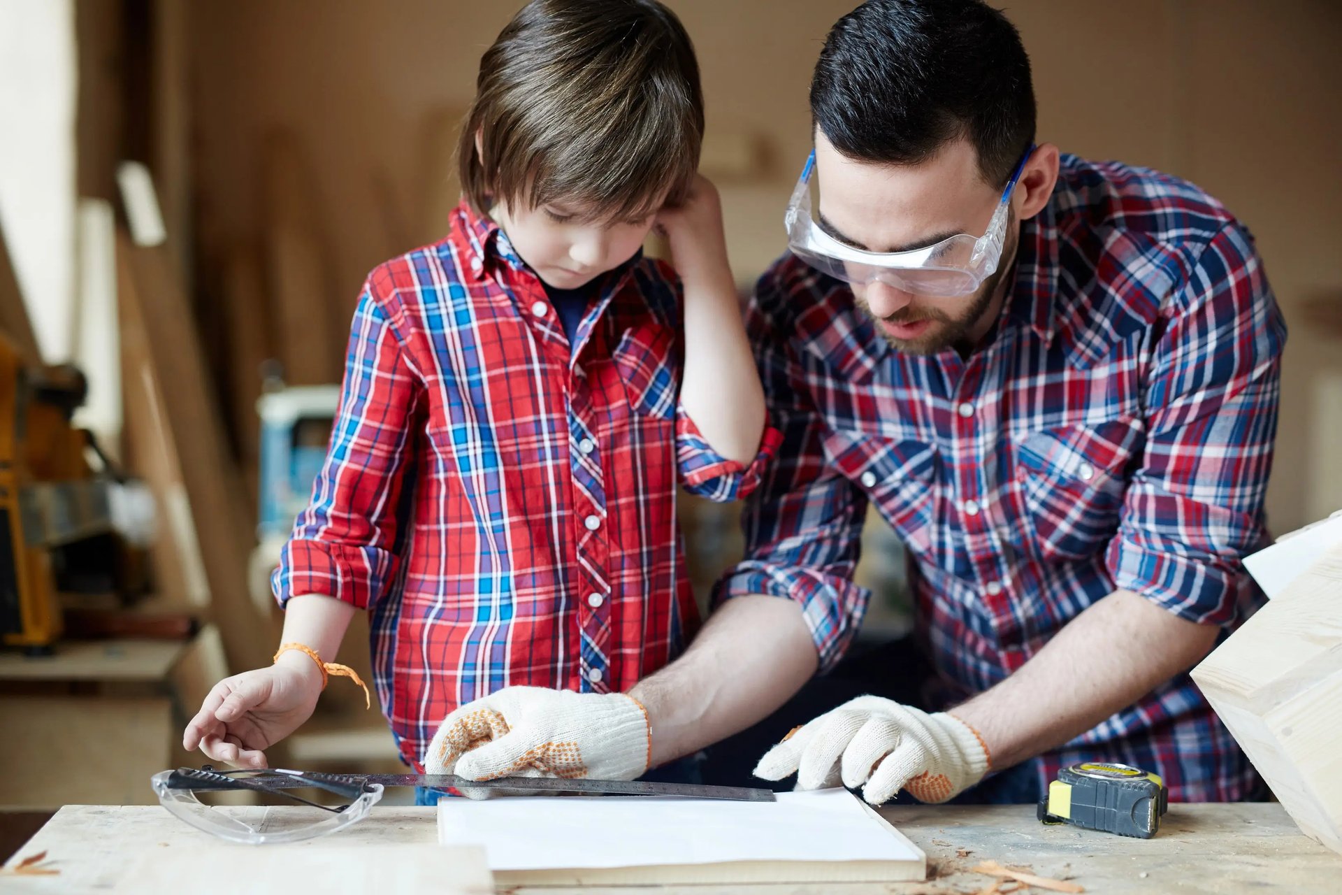 un père mesurant une planche de bois avec son fils