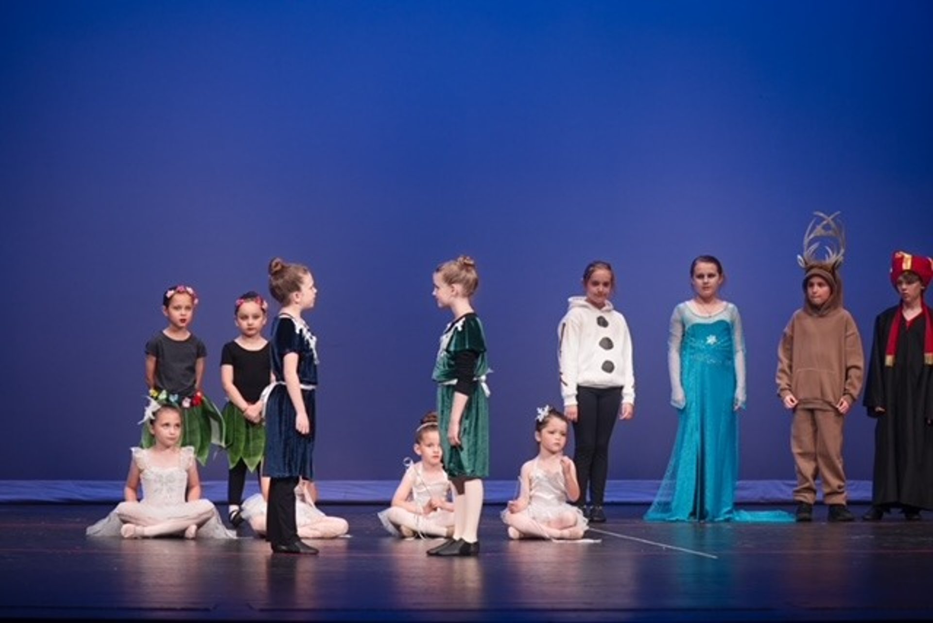 Kid actors in colorful costumes for Frozen Jr. on stage performing a song.