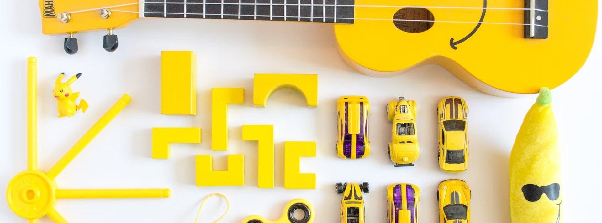 yellow ukulele, cars, emoji plush toy on white surface
