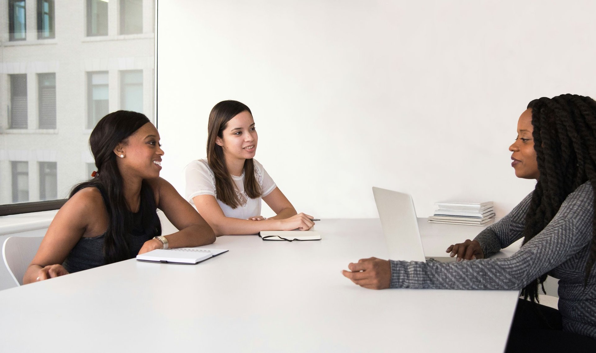 Three women of color having a business meeting in a white conference room with a window