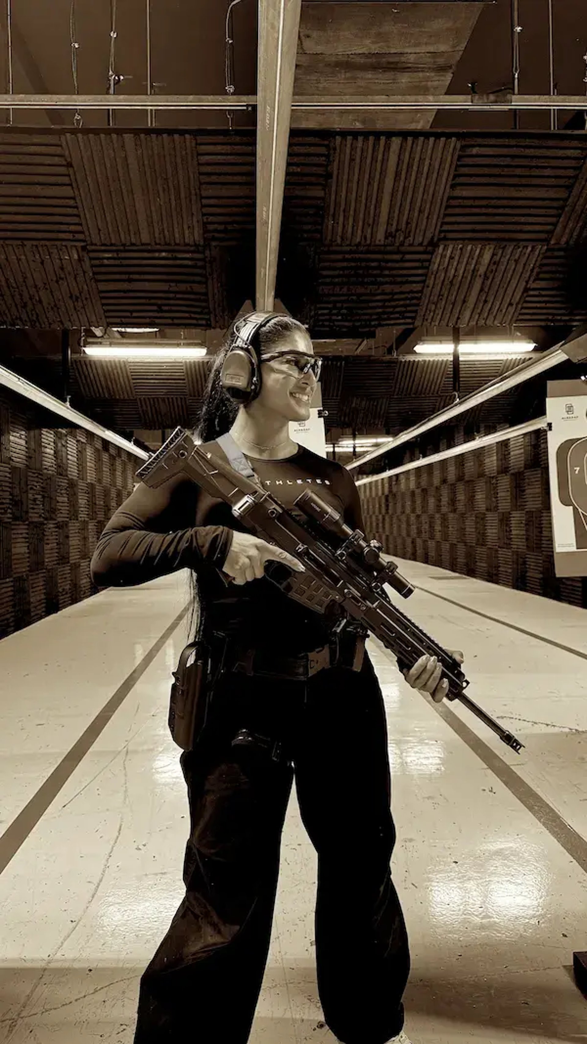 mais alhajri smiling while holding a rifle at an indoor shooting range