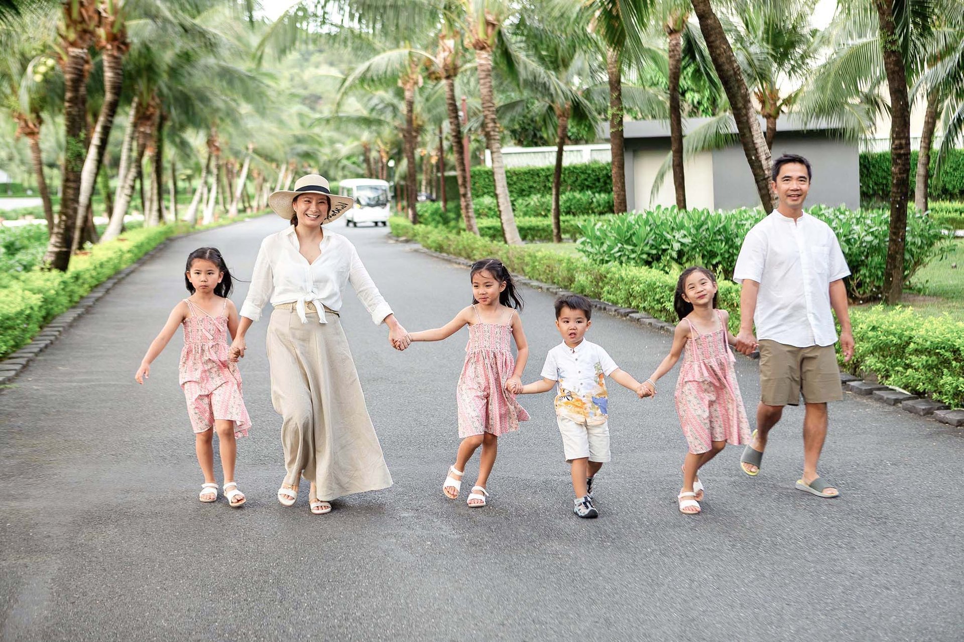 Family walking together on a palm-lined avenue at New World Resort, Khem Beach, Phu Quoc