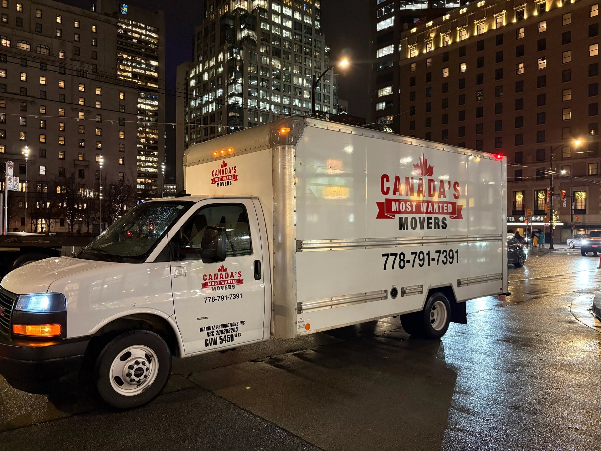 Canada’s Most Wanted Movers box truck operating in downtown Vancouver on a rainy evening.