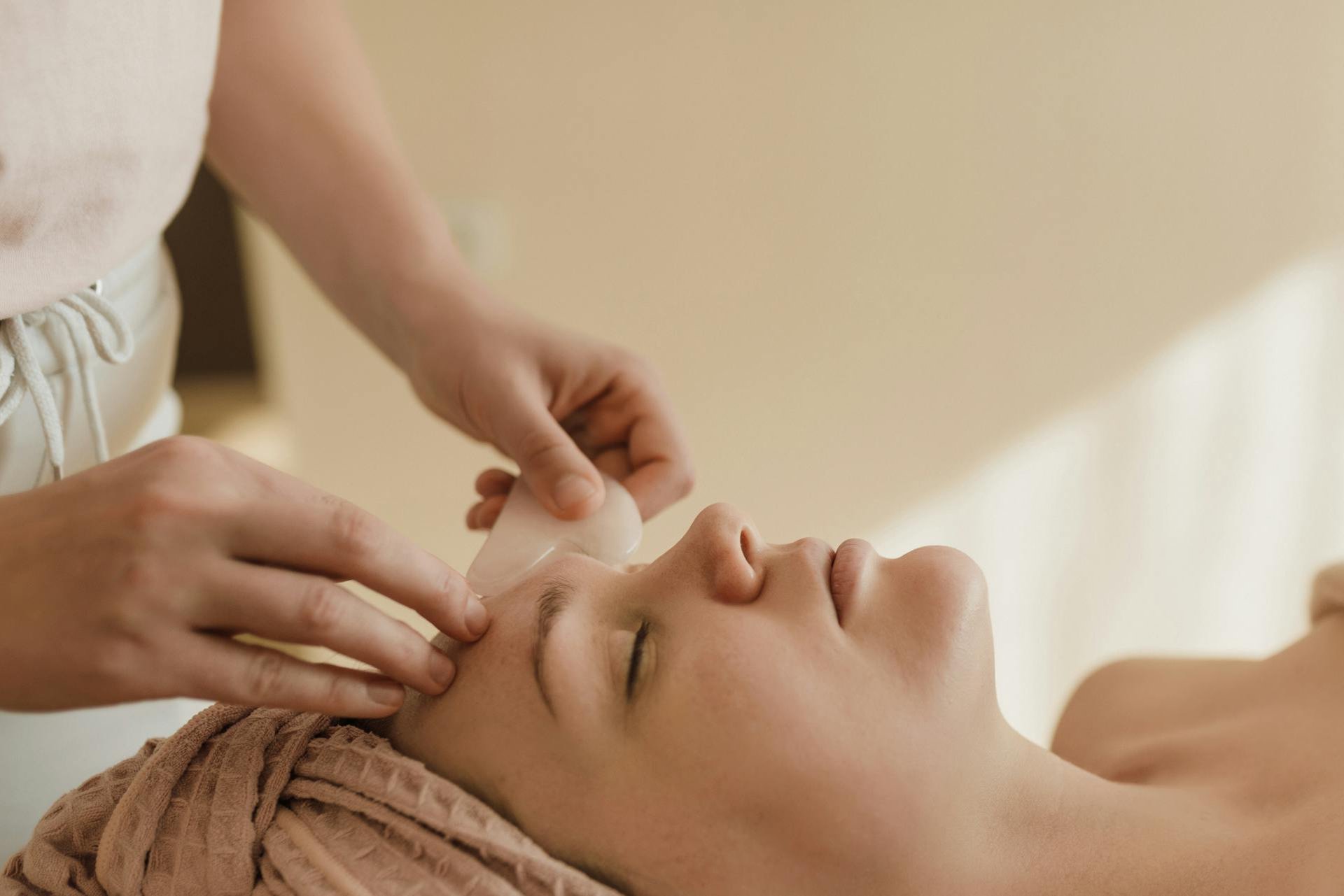 Mujer recibiendo exfoliación de espalda con sales rosas en un spa, rodeada de velas encendidas y ambiente relajante.