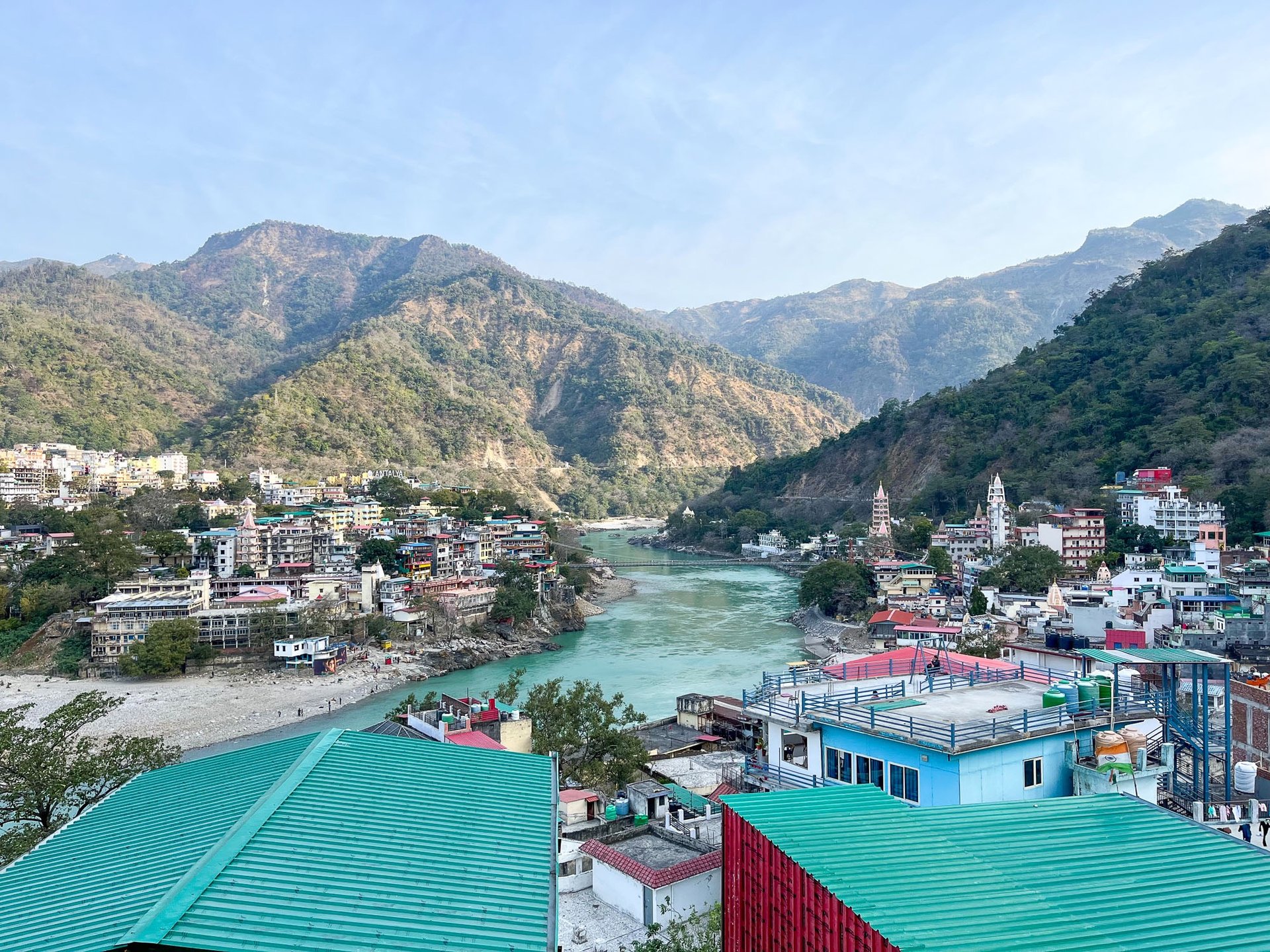 Scenic rooftop view overlooking the mountains and the cityscape of Rishikesh, India, under a clear sky.