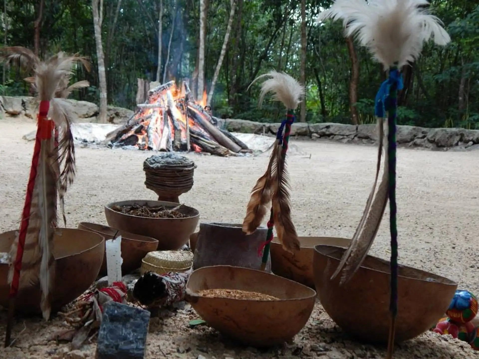 Ofrendas rituales tradicionales y plumas frente a un fuego ceremonial de temazcal en la selva maya.