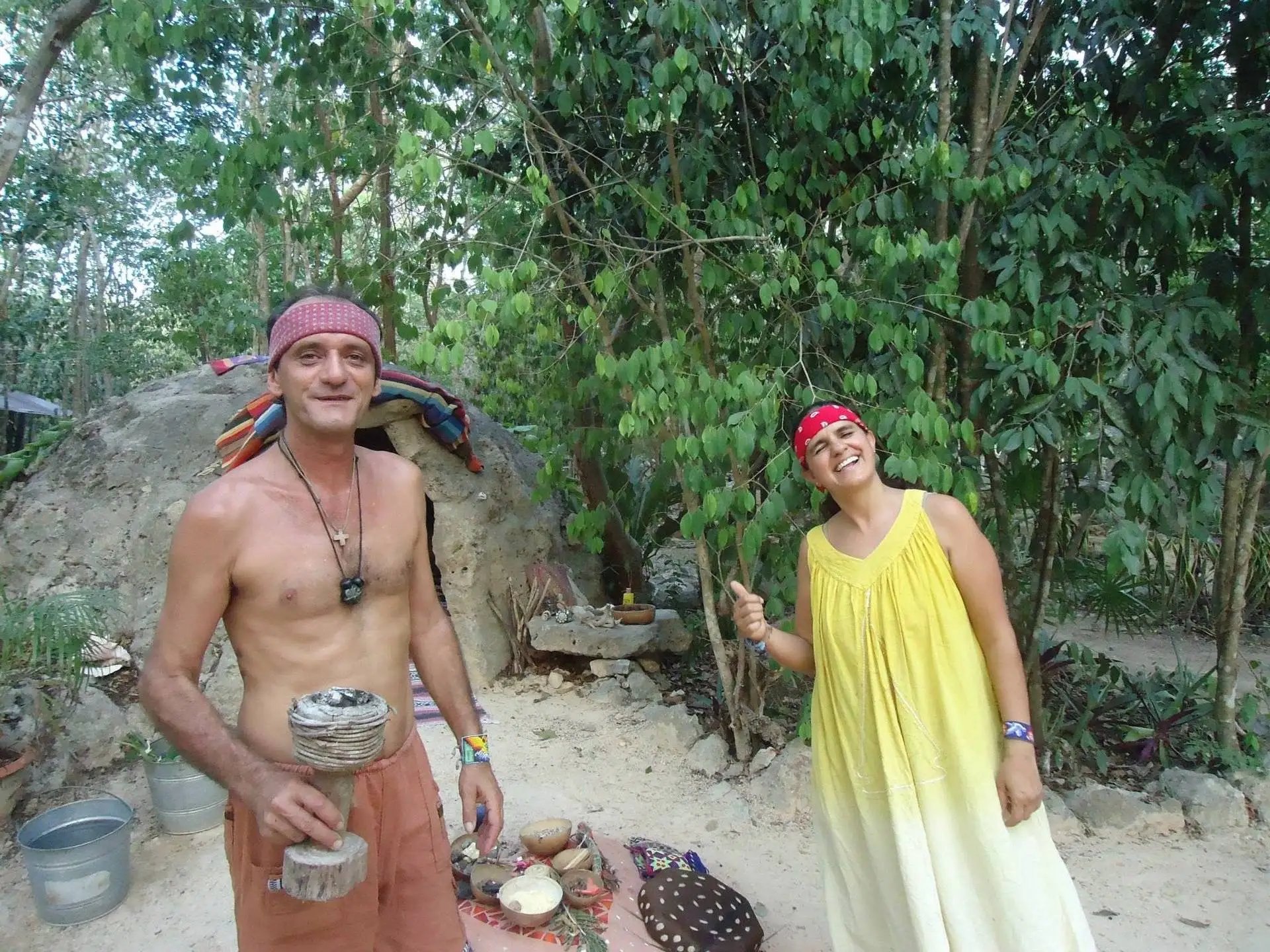 Un hombre y una mujer de pie junto a un temazcal tradicional durante un retiro espiritual en la selva.