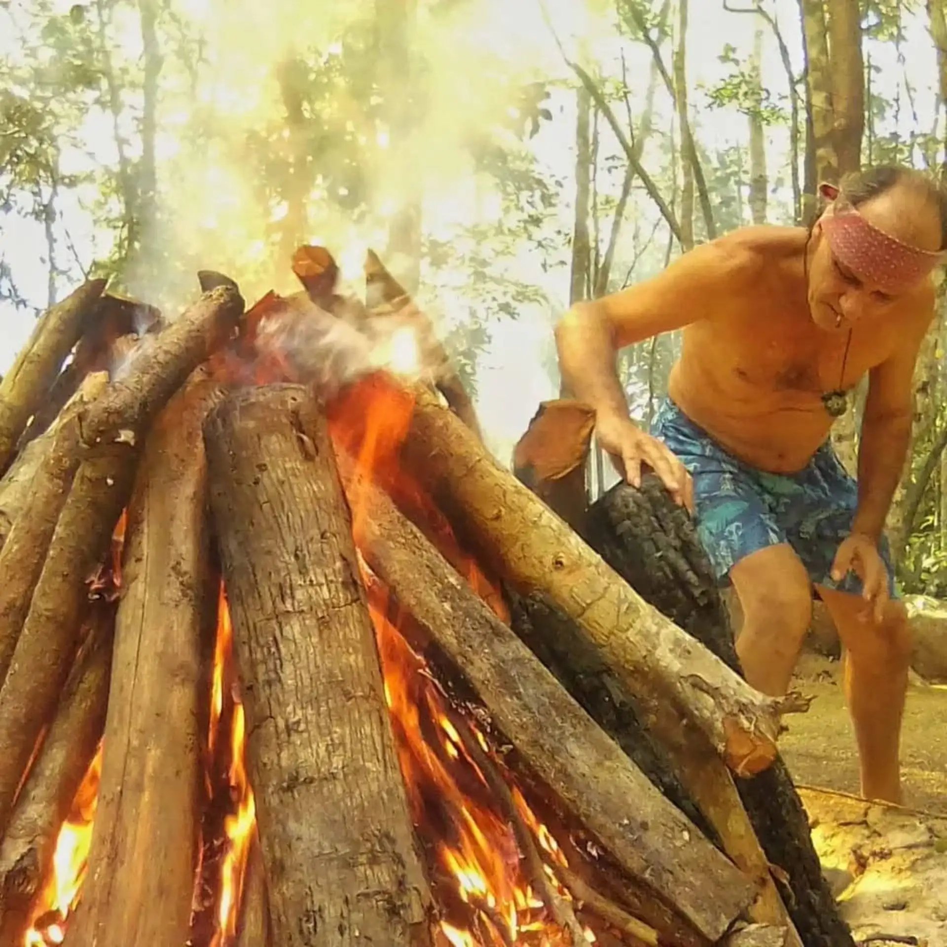 UUn hombre con una cinta en la cabeza atiende el fuego de un temazcal al aire libre, en la selva maya