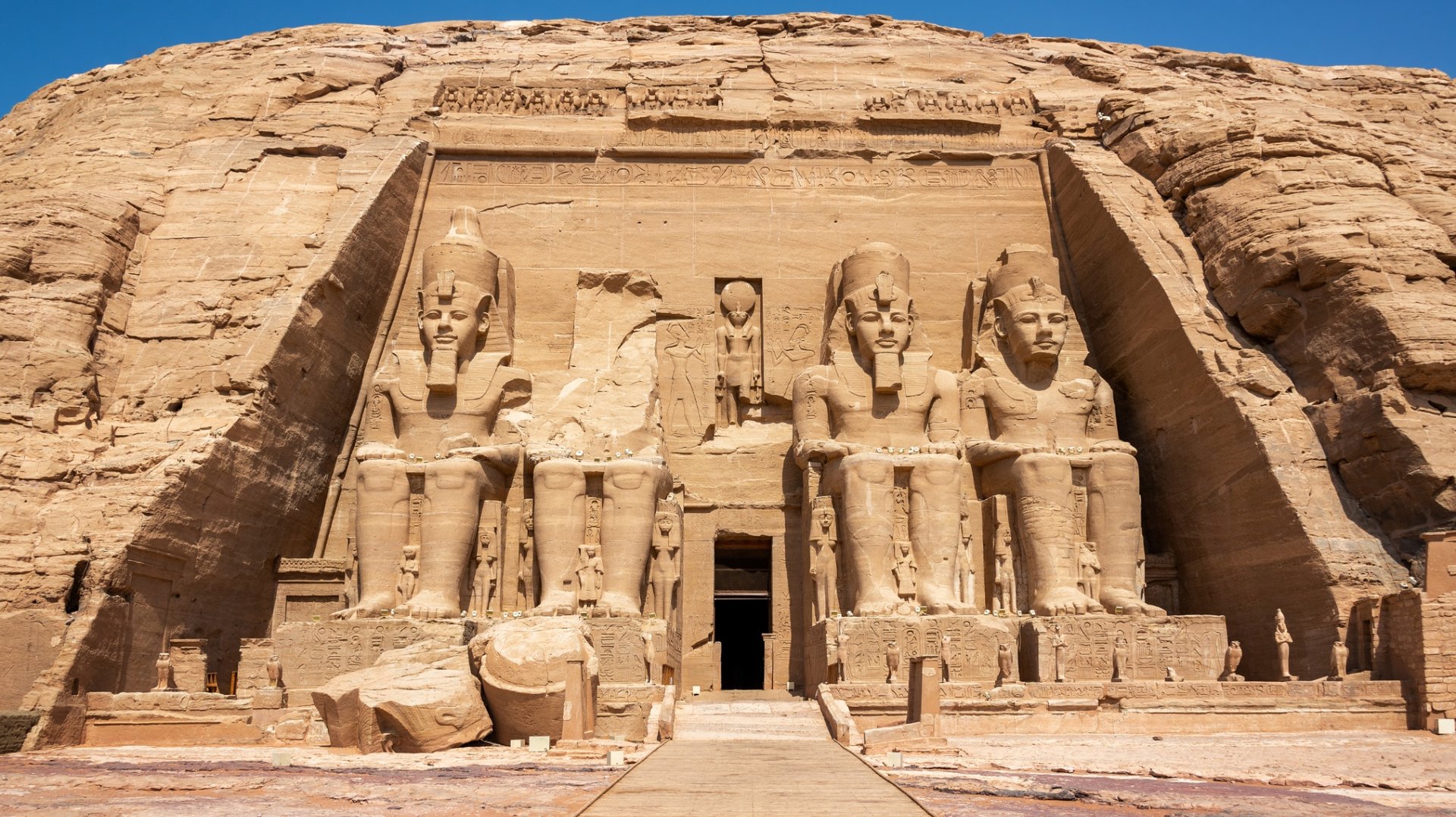 a stone wall with carvings with Abu Simbel temples in the background