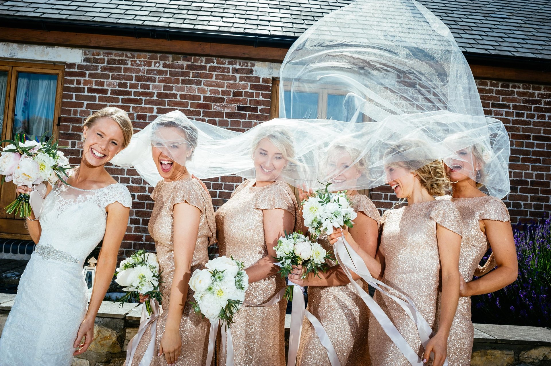 Bridal party laughing as wind lifts the bride’s veil at Rosedew Farm wedding, fun South Wales photography