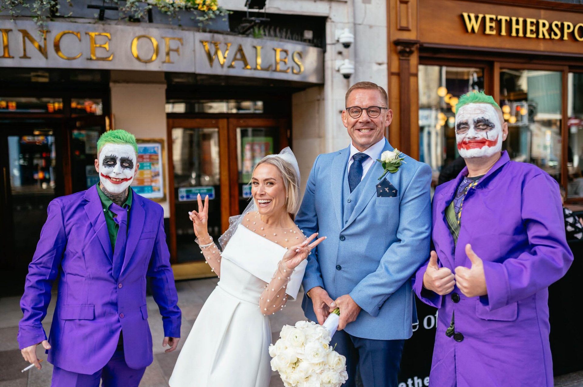 Bride and groom outside Prince of Wales Cardiff, joined by two guests dressed as the Joker in purple suits and face paint.