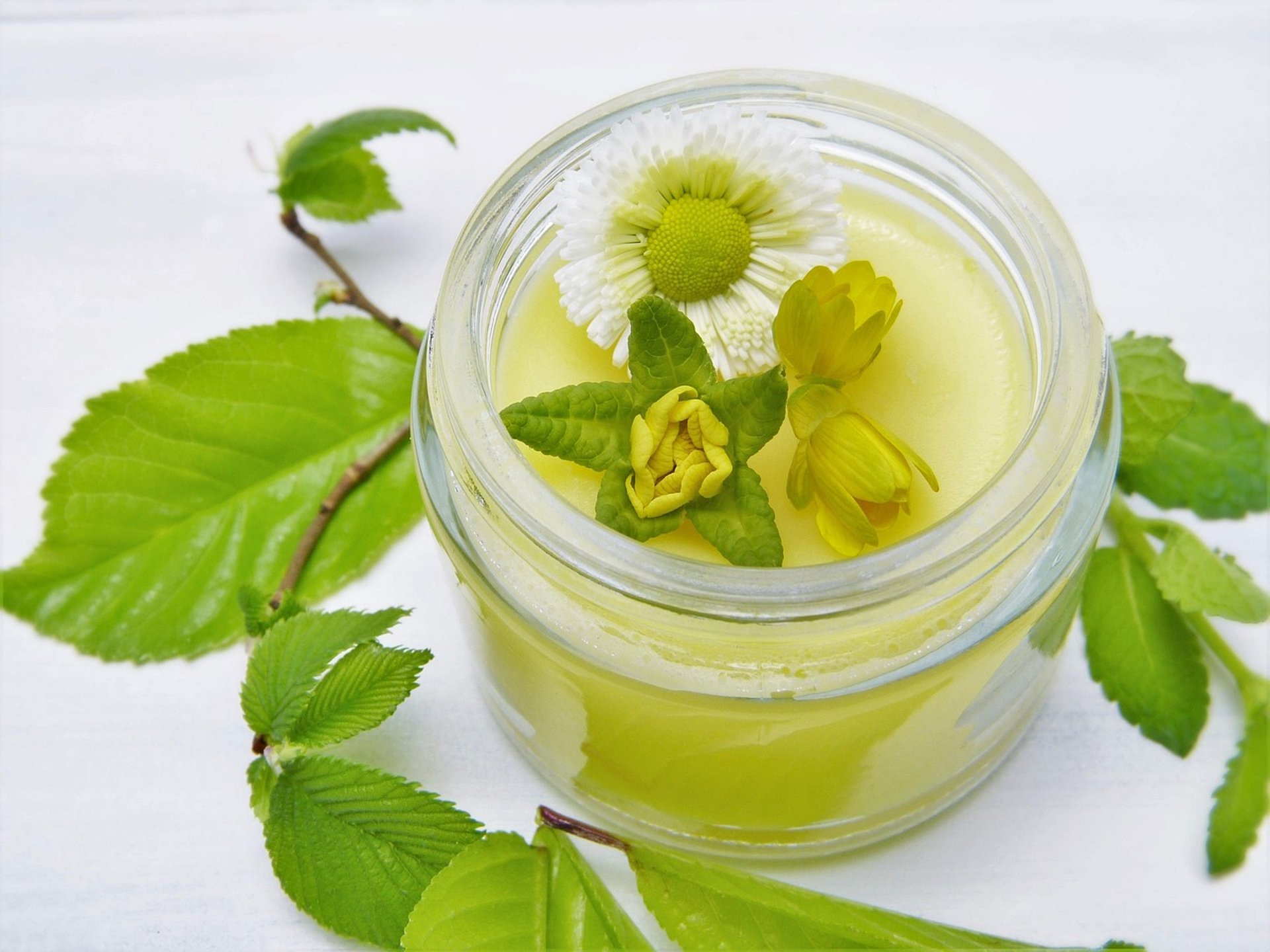 Pote de creme natural amarelo decorado com flores e folhas verdes, representando cosméticos artesanais à base de ingredientes