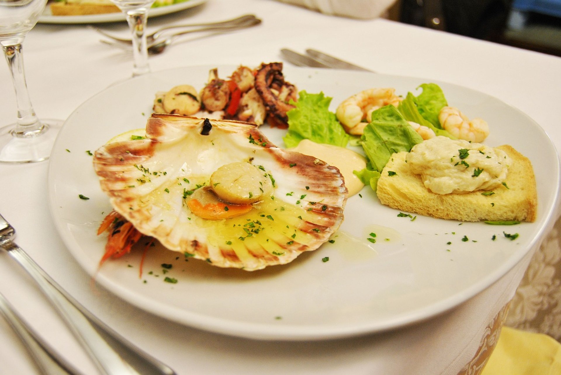 Prato refinado de frutos do mar com vieira servida na concha, camarões, polvo grelhado, torrada com creme e folhas verdes, ap