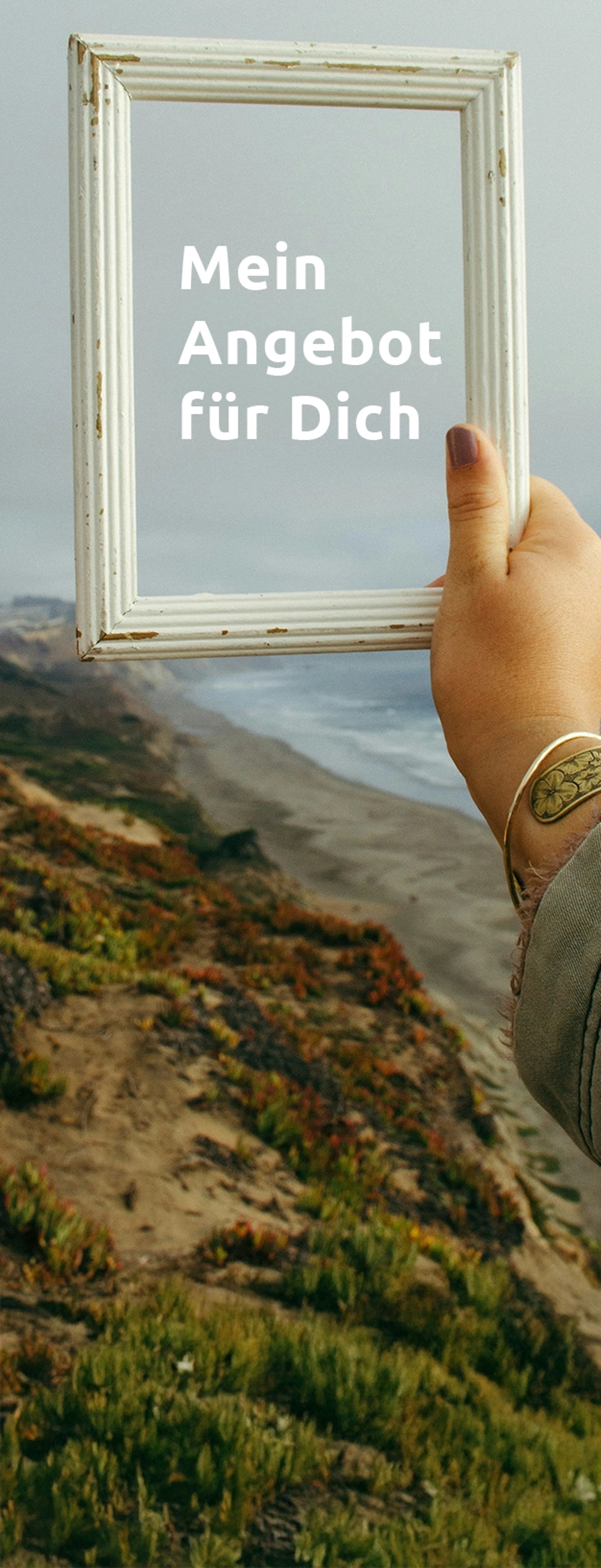 person holding rectangular white photo frame standing on rock formation near body of water