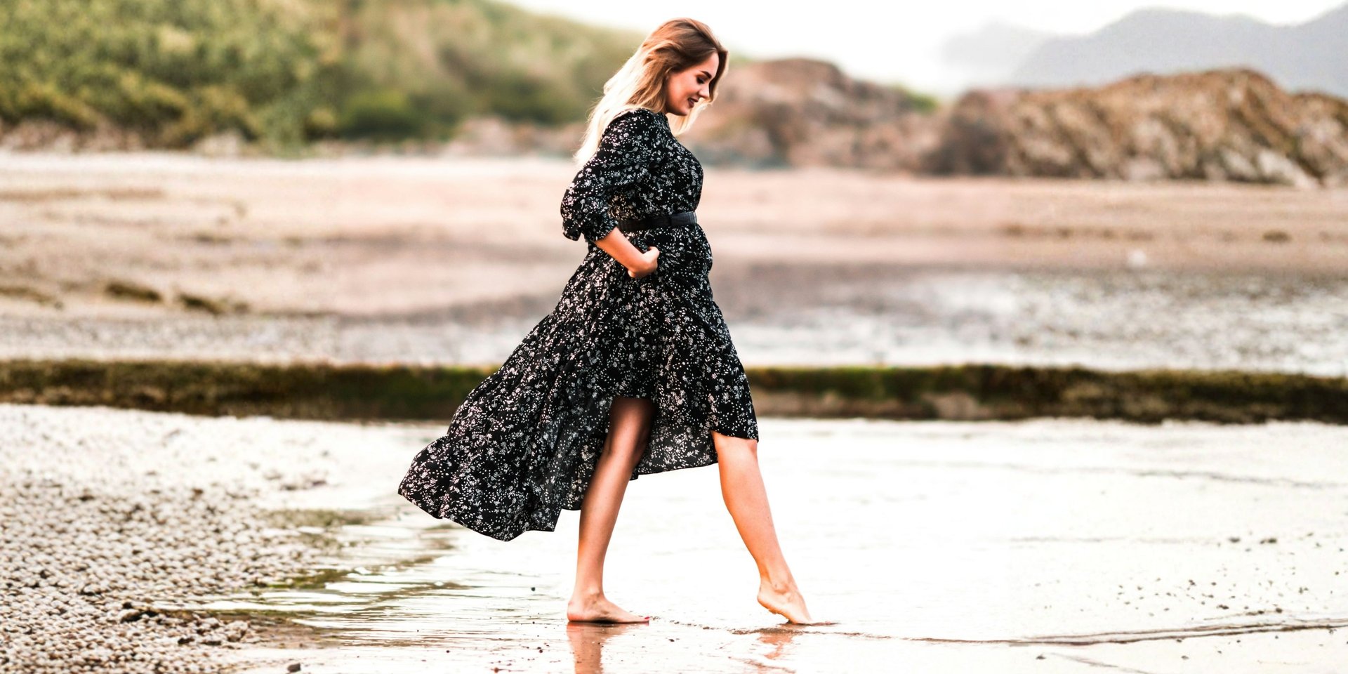 woman in black and white floral dress standing on seashore during daytime