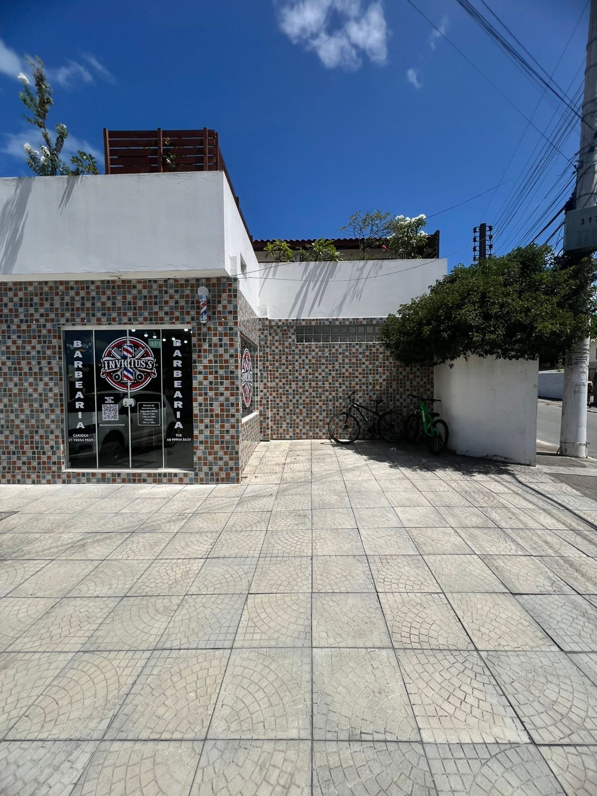 Foto da fachada da barbearia, mostrando a porta de entrada, logo e a área da frente para estacionamento