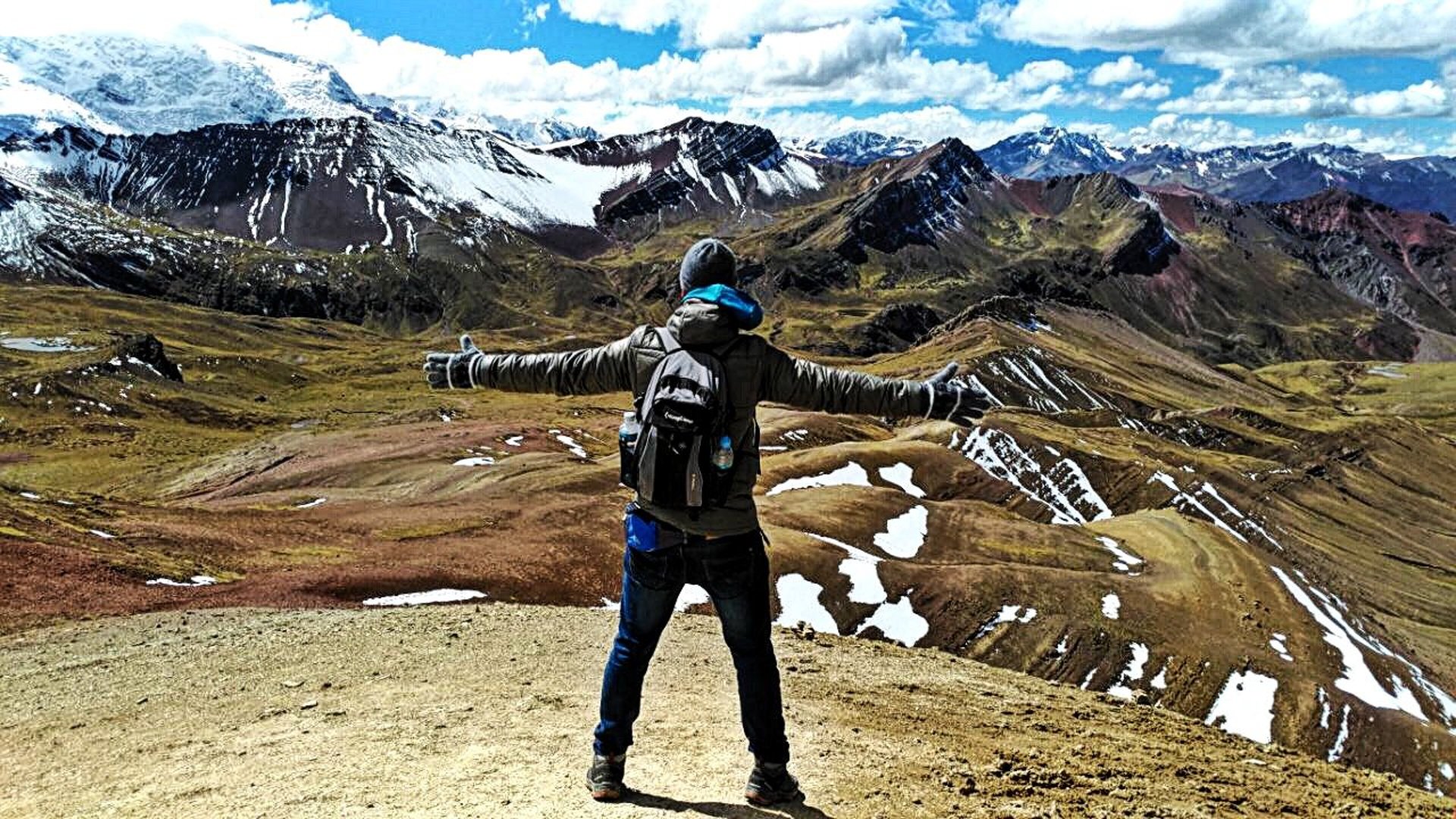 Randonneur au sommet de Vinicunca à 5000 m, vue panoramique sur les Andes enneigées et les reliefs colorés de la montagne de